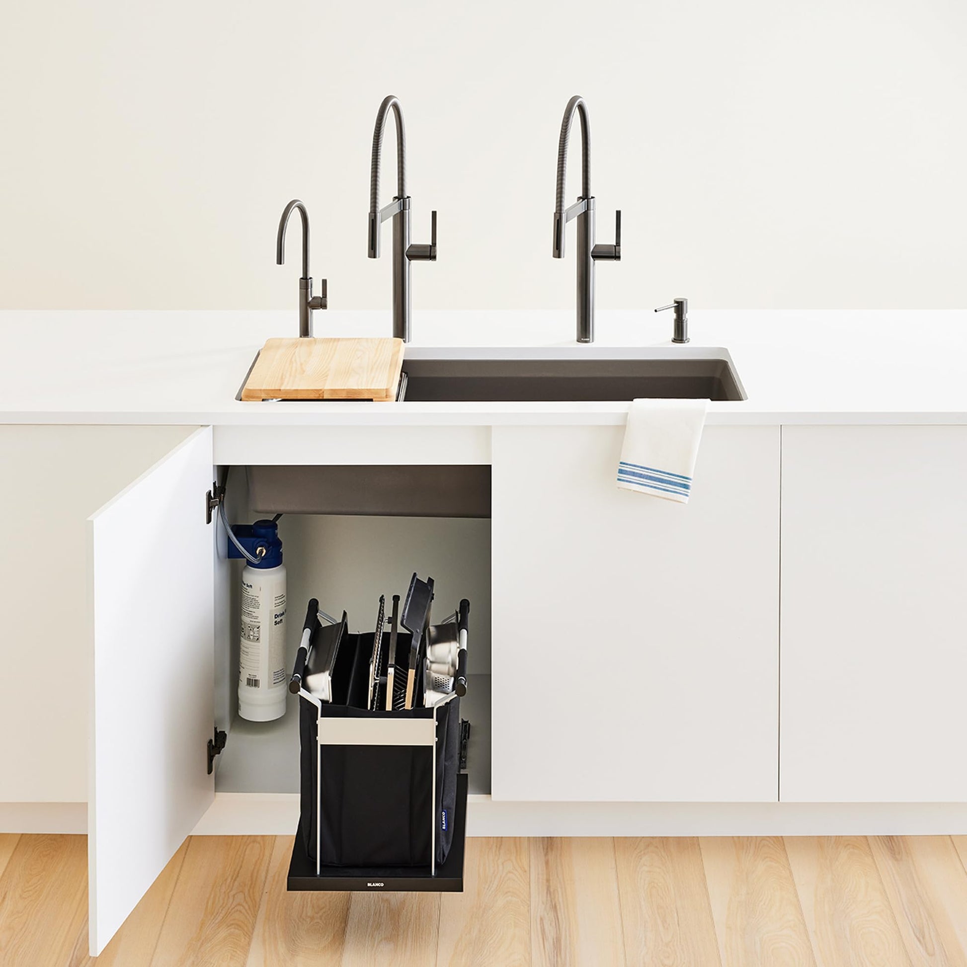 Black pull-out sink organizer with knife block and utensil storage installed under kitchen sink with faucets.
