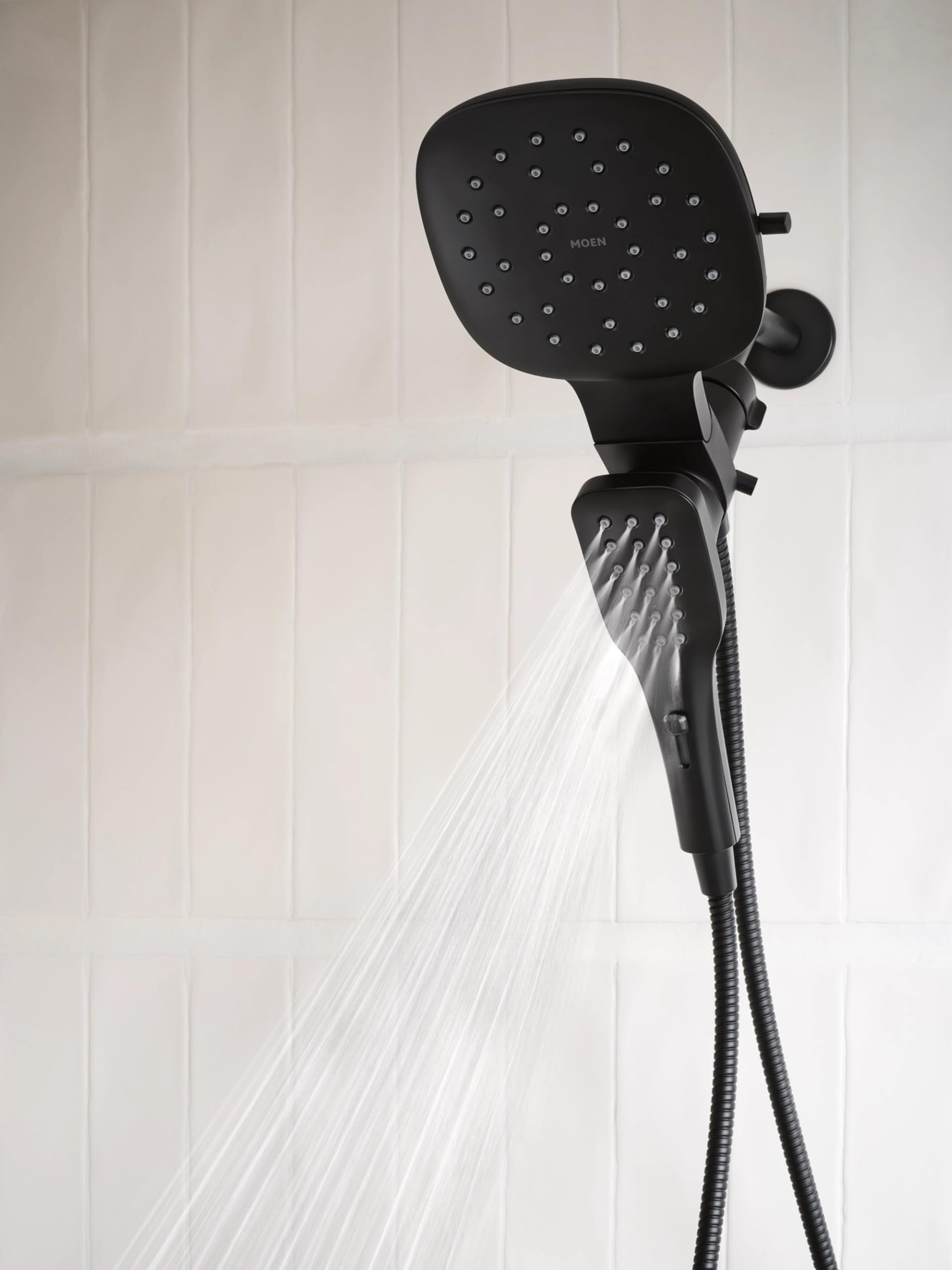 Matte black square rain shower head with multiple spray jets mounted above detachable hand shower with hose.