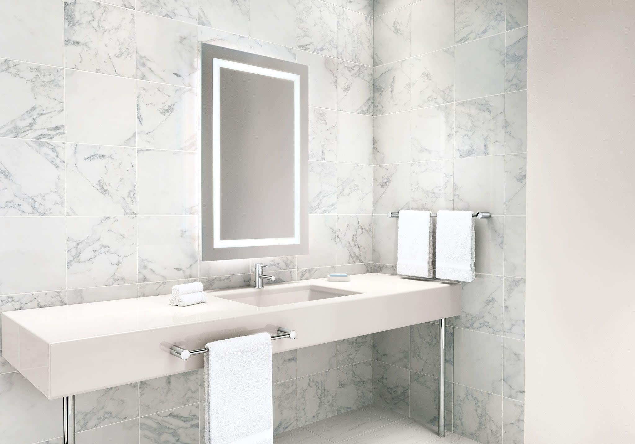 Chrome single-handle bathroom faucet with low-profile spout mounted on white vanity in marble tiled bathroom.