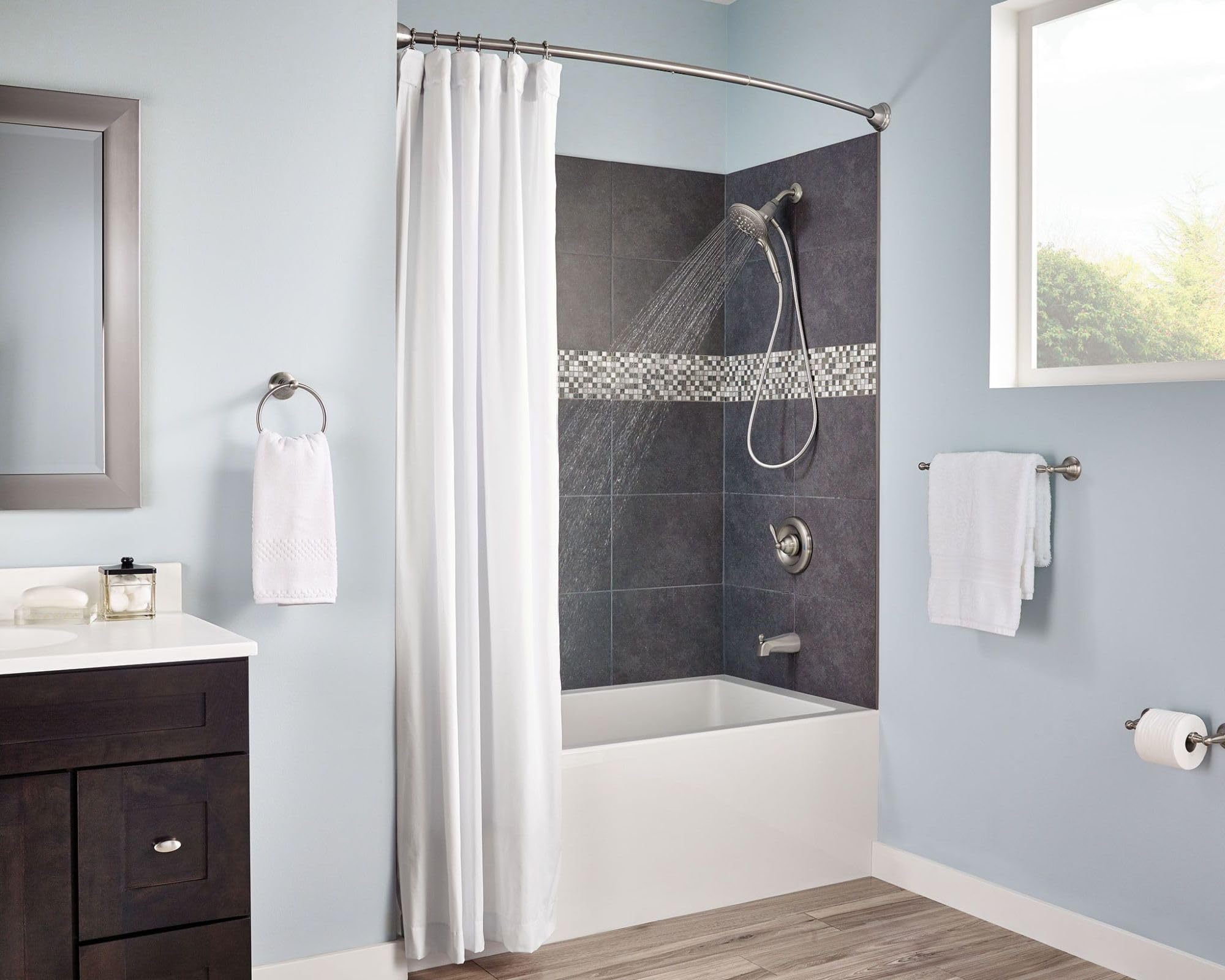 Brushed nickel wall-mounted towel ring holding a rolled white hand towel in a bathroom.