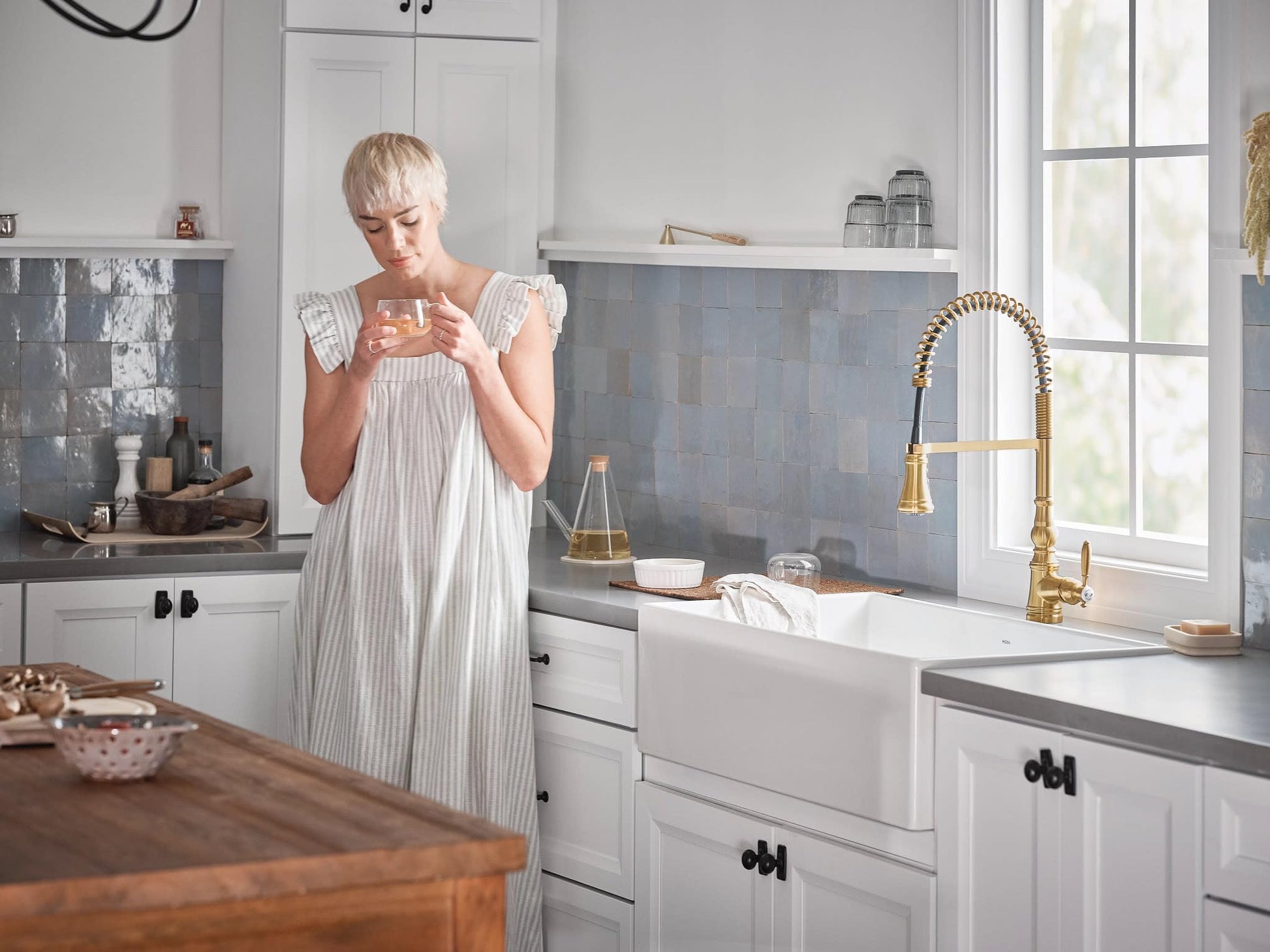 Brushed gold pulldown kitchen faucet with single handle and coiled spring hose mounted above white farmhouse sink.