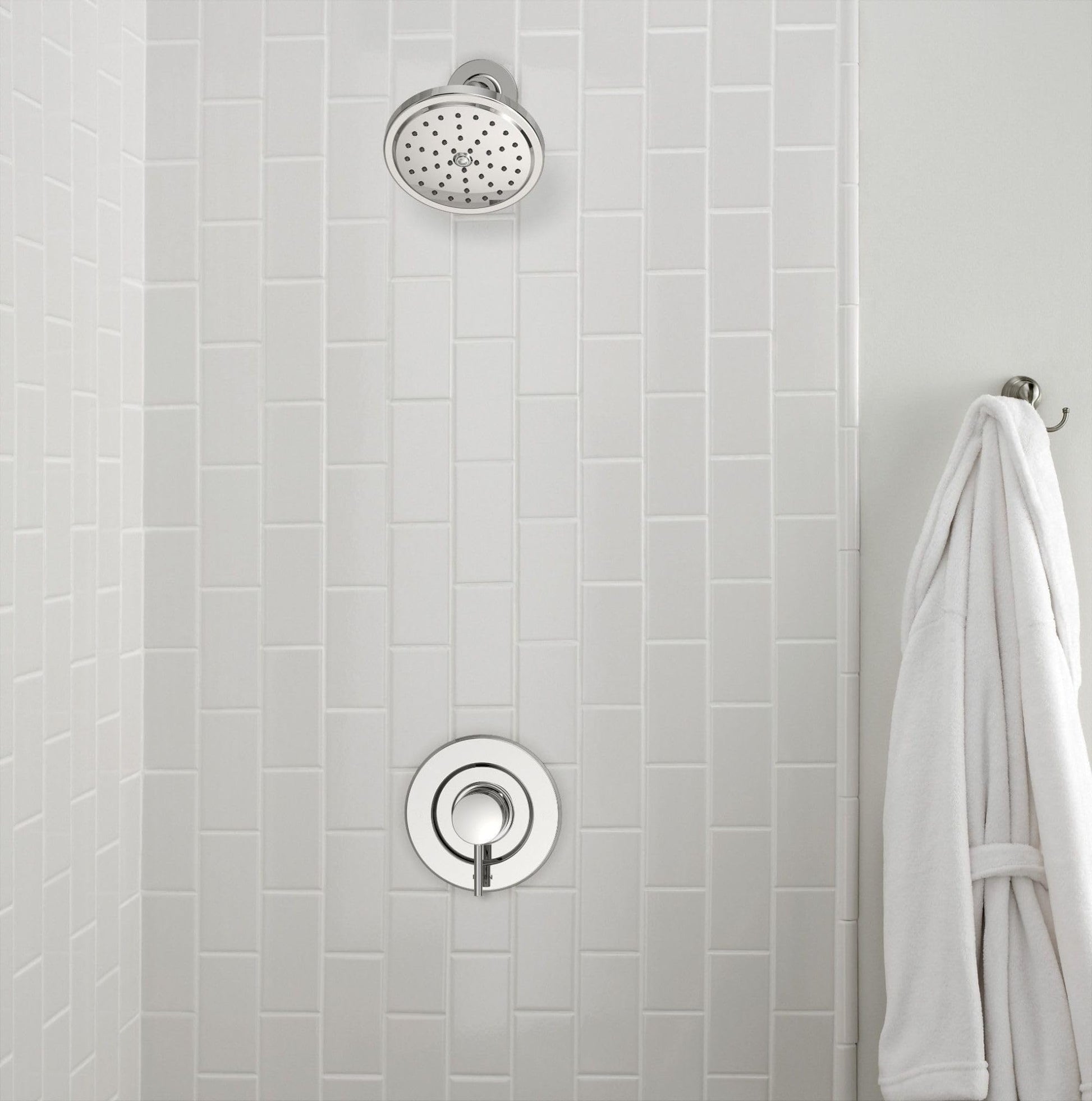 Chrome shower system with circular showerhead and round trim ring mounted on white subway tile wall.