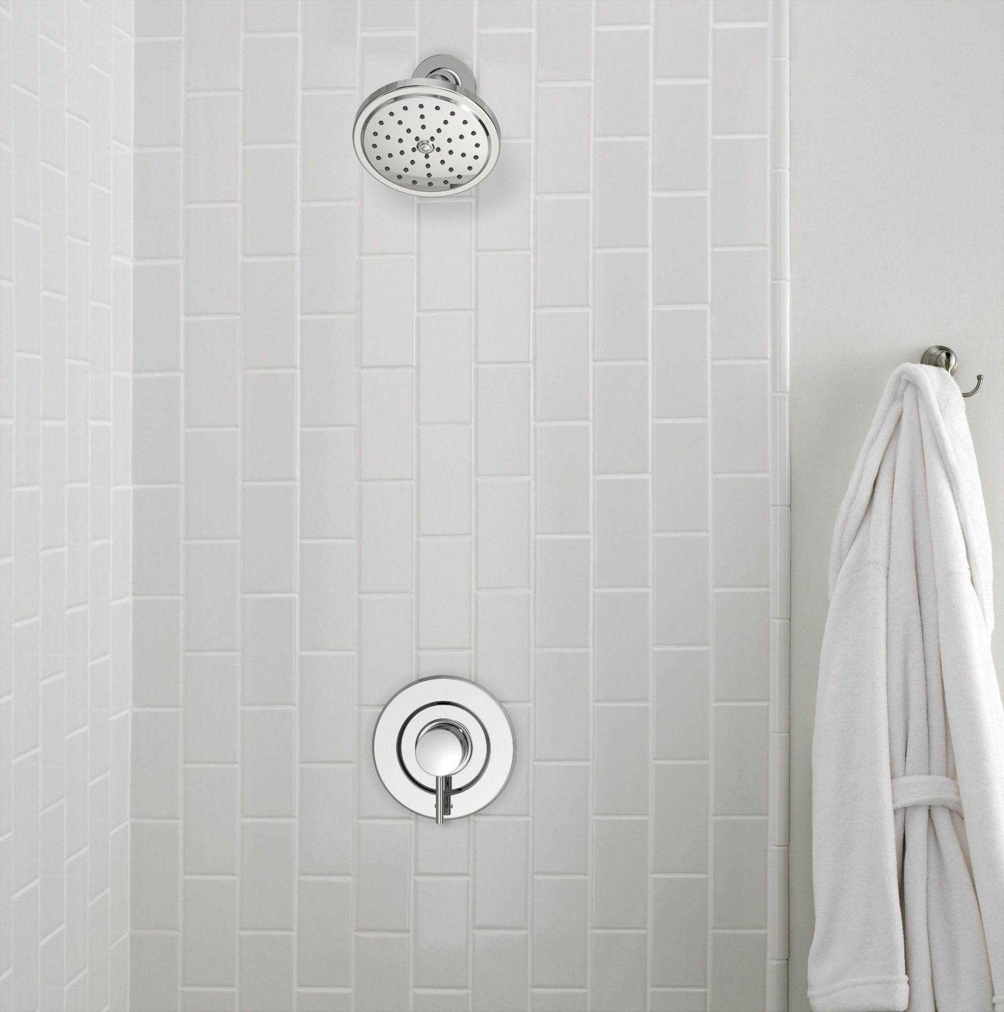 Chrome shower system with circular showerhead and round trim ring mounted on white subway tile wall.