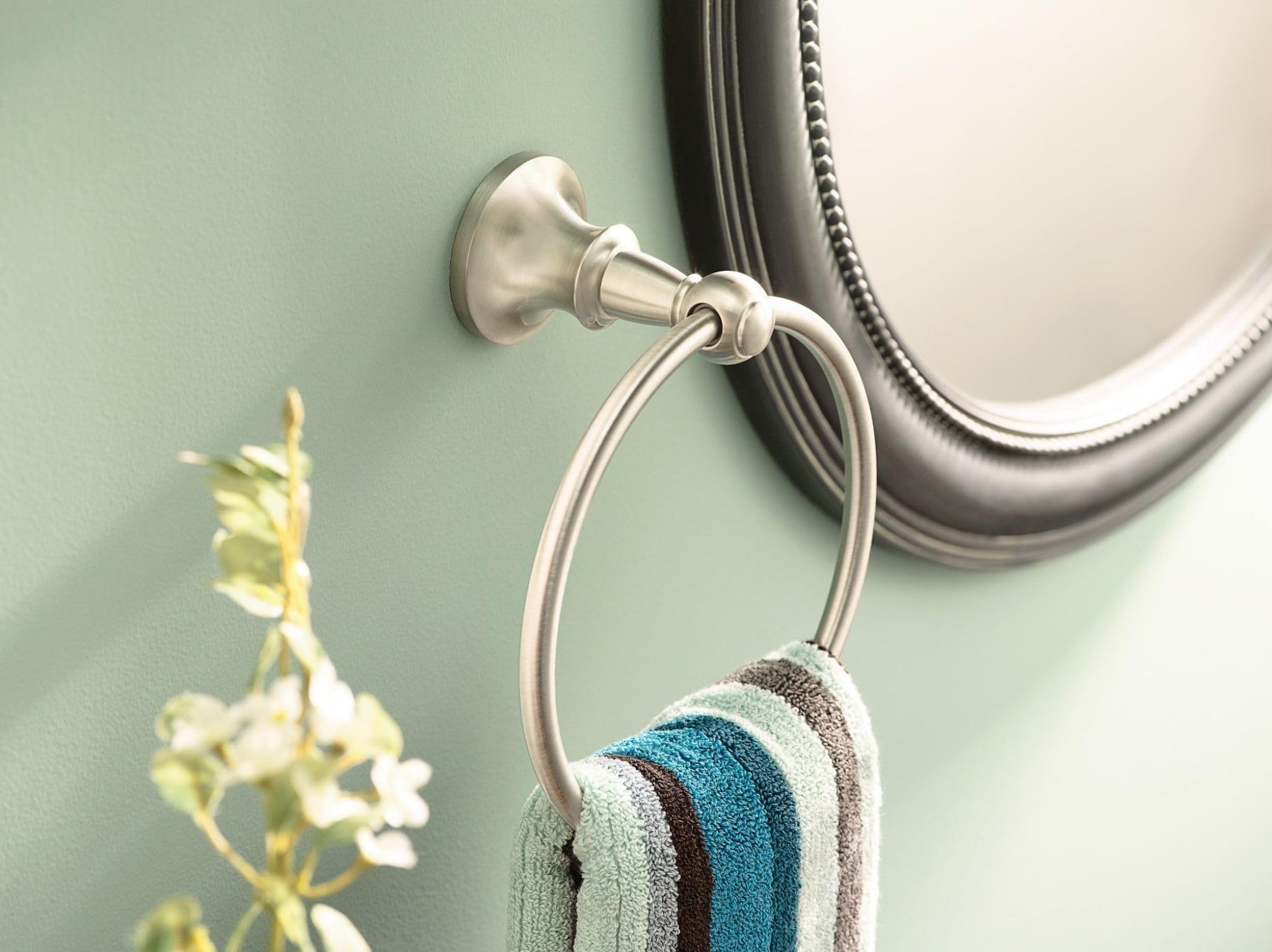 Brushed nickel wall-mounted towel ring with circular ring holding a striped towel, mounted on green wall.