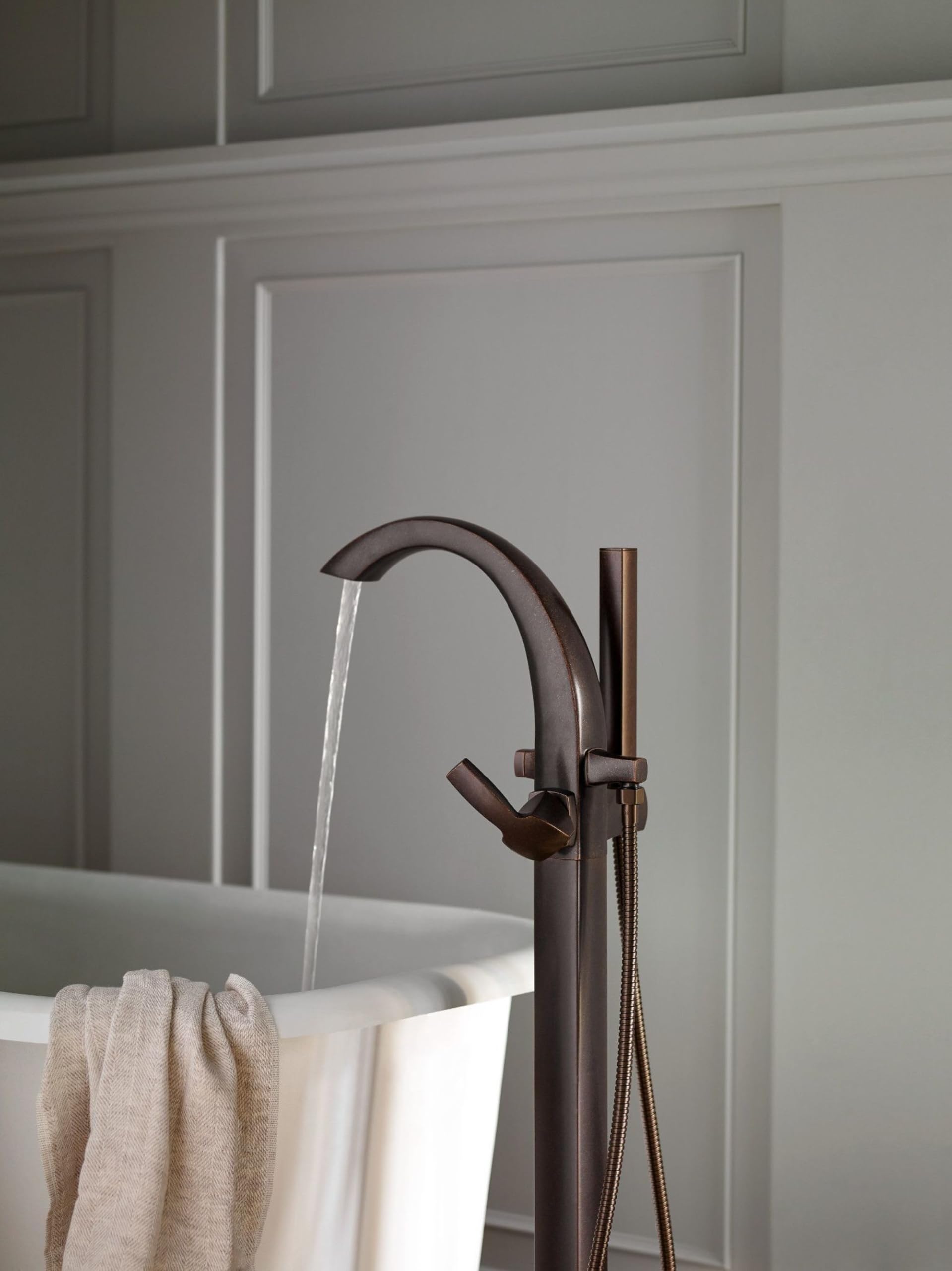 Oil rubbed bronze freestanding tub filler with curved spout, single lever handle, and detachable handshower on hose.