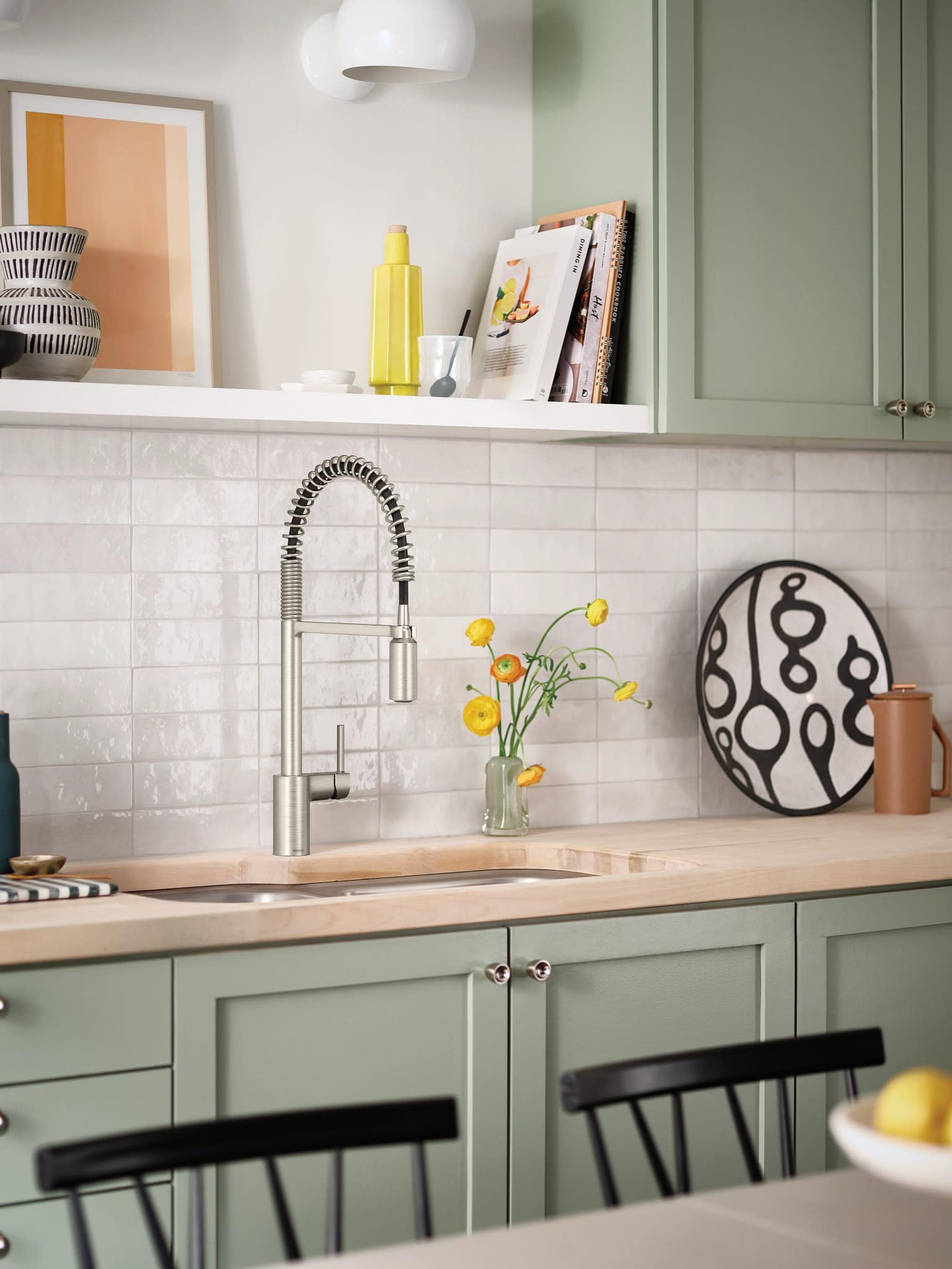 Stainless steel pull-down kitchen faucet with coiled hose and cylindrical spout mounted above sink in white subway tile backs