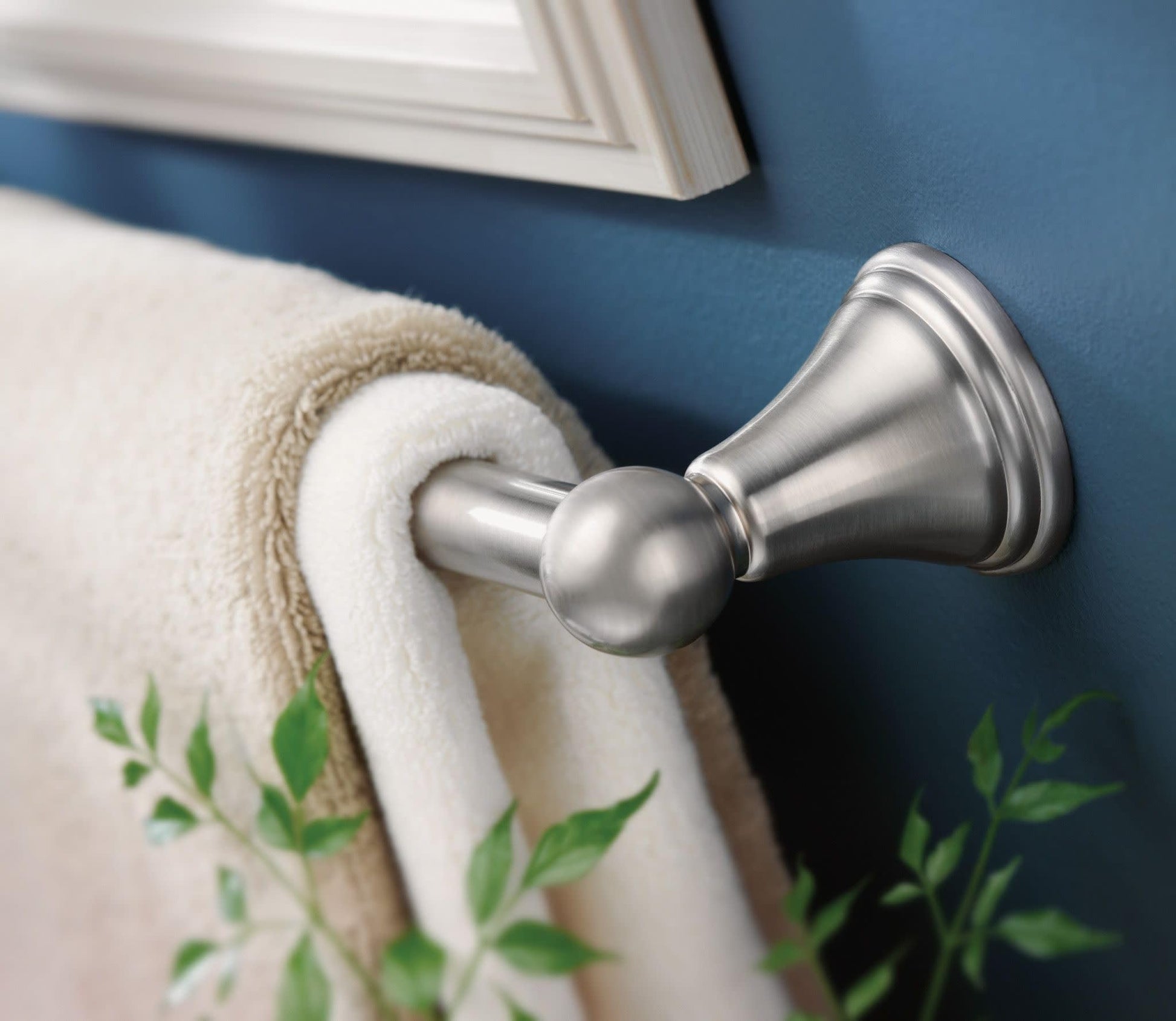 Brushed nickel towel bar mounted on blue wall with rolled towel and decorative plant.