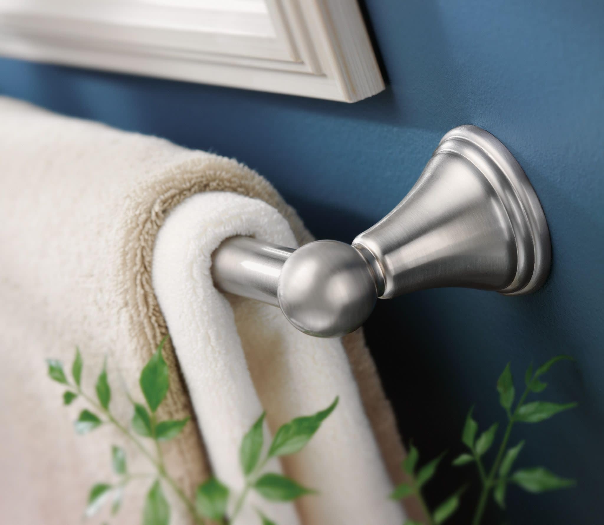 Brushed nickel towel bar mounted on blue wall with rolled towel and decorative plant.