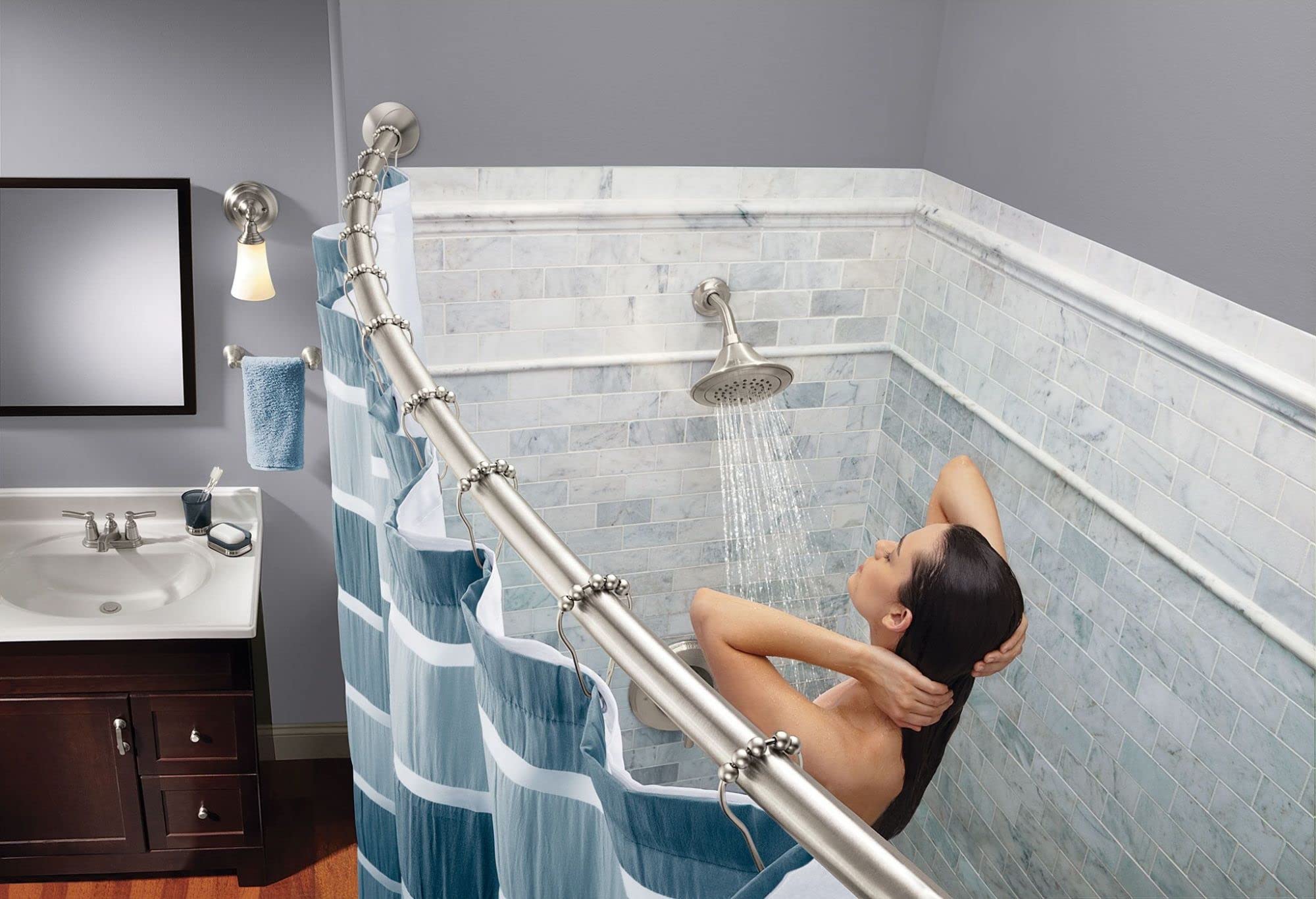 Brushed nickel curved shower rod with decorative rings installed in bathroom with white subway tile surround and blue striped