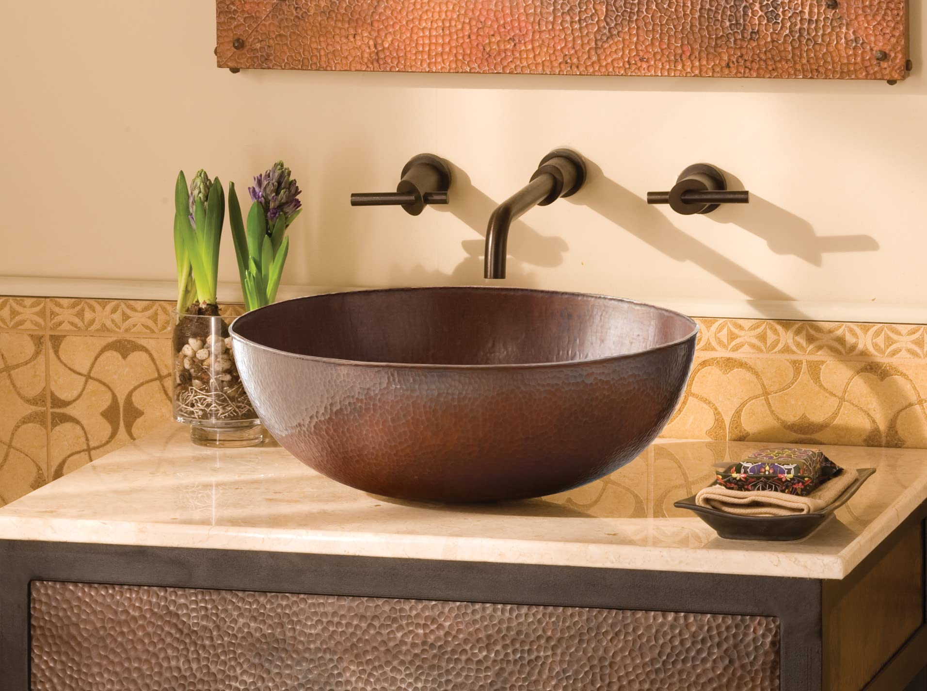 Antique copper oval bathroom sink with hammered texture on marble countertop, three-handle wall faucet.