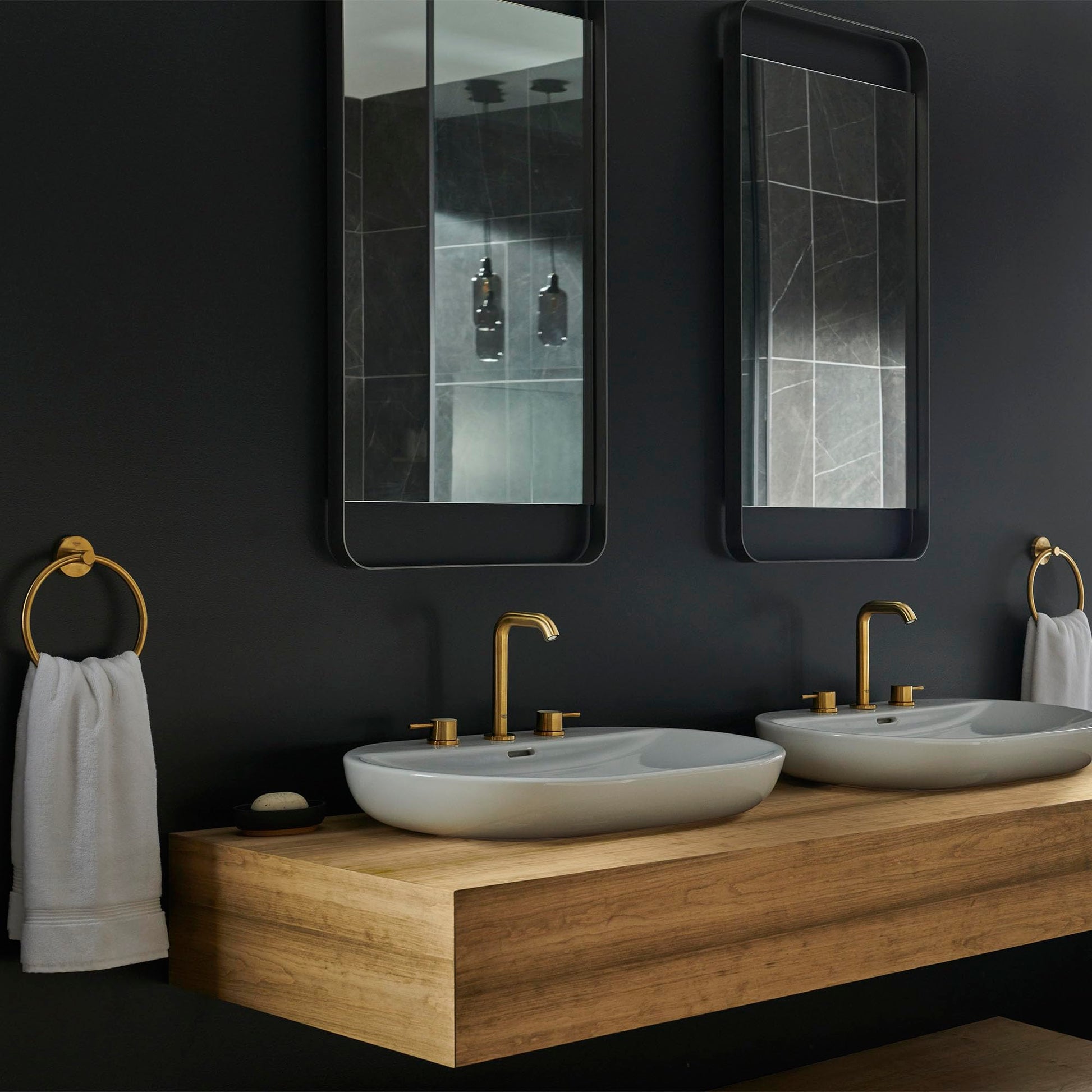 Brushed gold widespread bathroom faucet with two handles mounted on wooden vanity between white oval sinks.