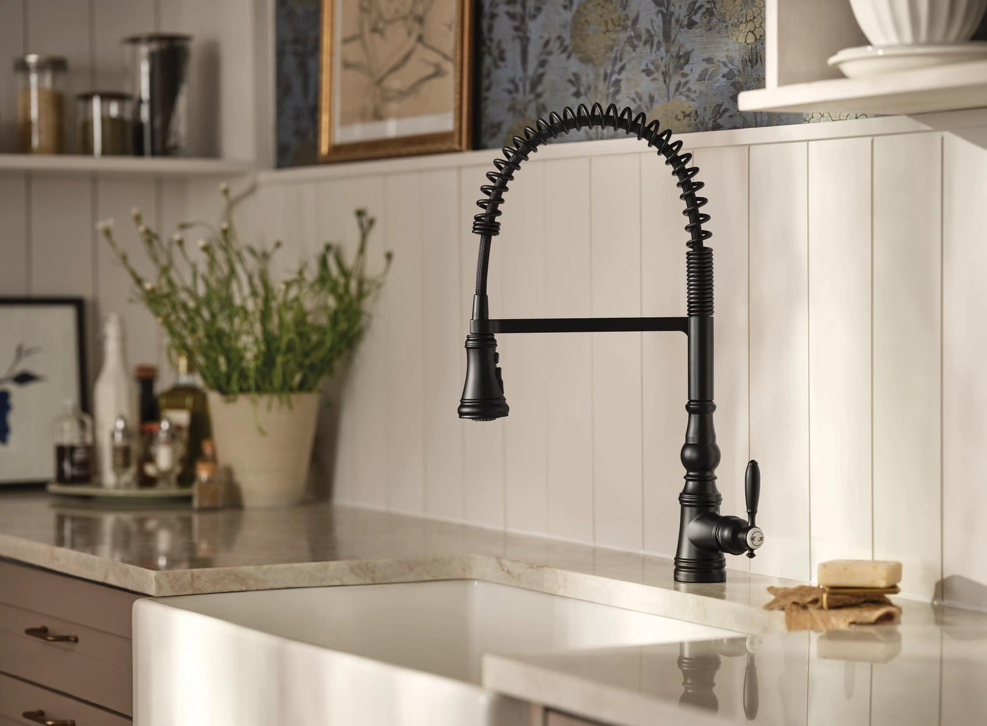 Matte black kitchen faucet with coiled pull-down sprayer and sensor control mounted above white farmhouse sink.