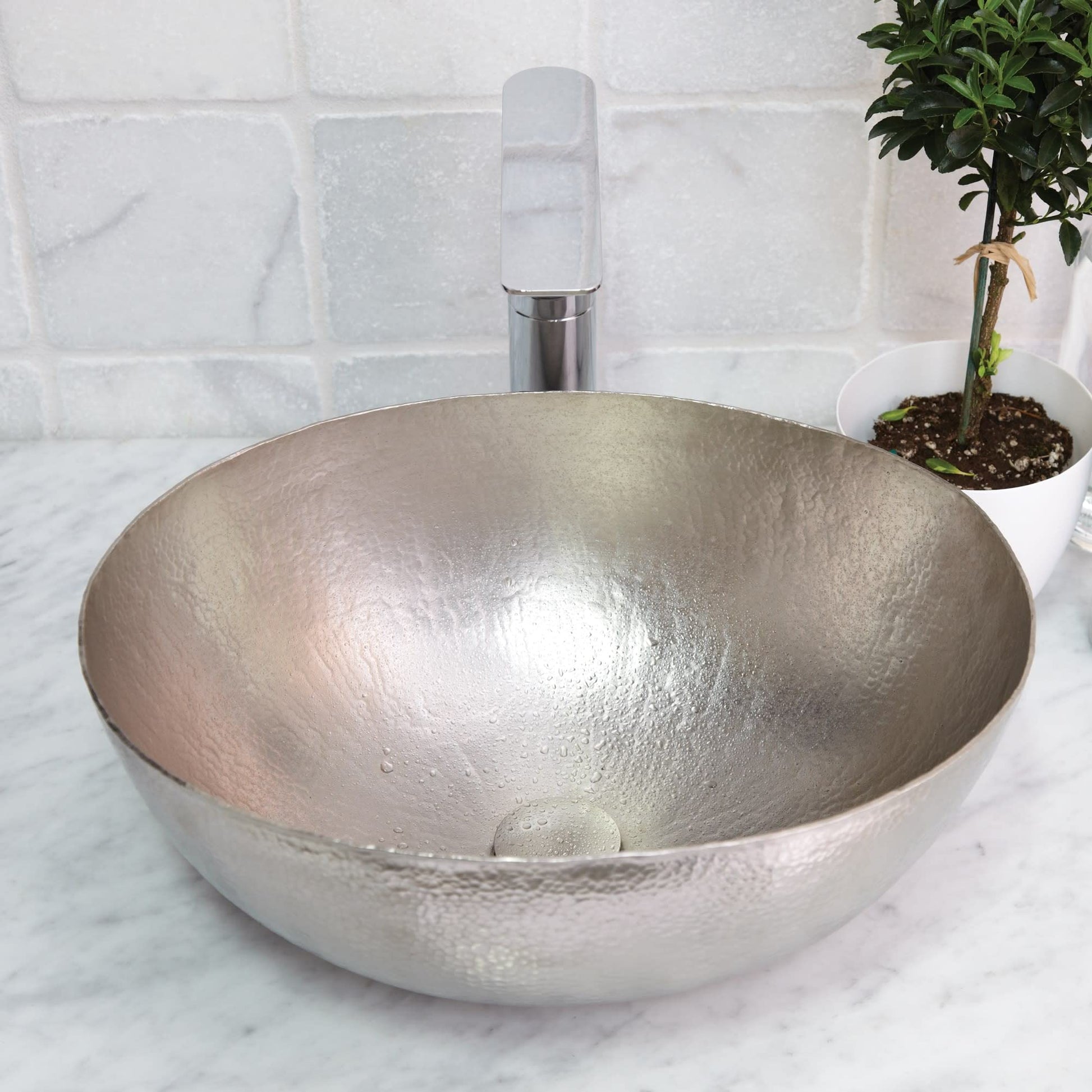 Oval copper sink with hammered antique finish and chrome faucet on marble countertop.