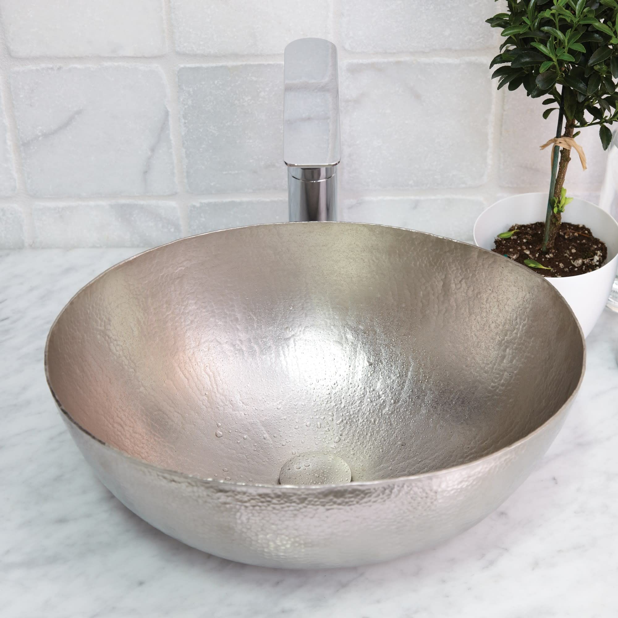 Oval copper sink with hammered antique finish and chrome faucet on marble countertop.