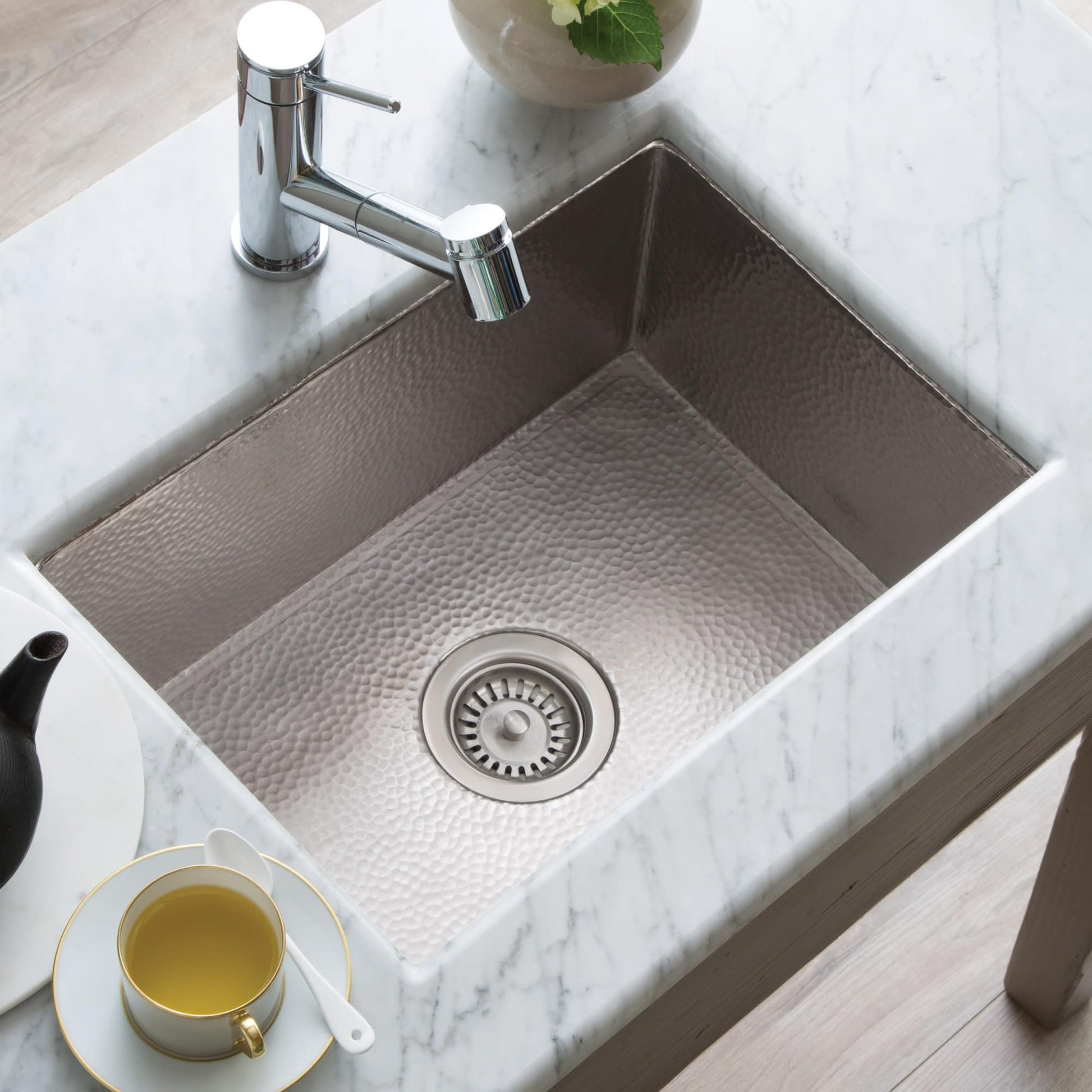 Rectangular copper kitchen sink with hammered finish and chrome faucet mounted on marble countertop.