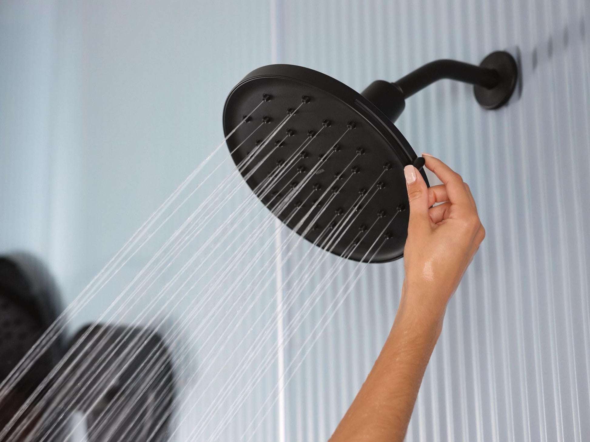Matte black circular rainshower head with multiple spray jets, mounted on adjustable arm, dispensing water.