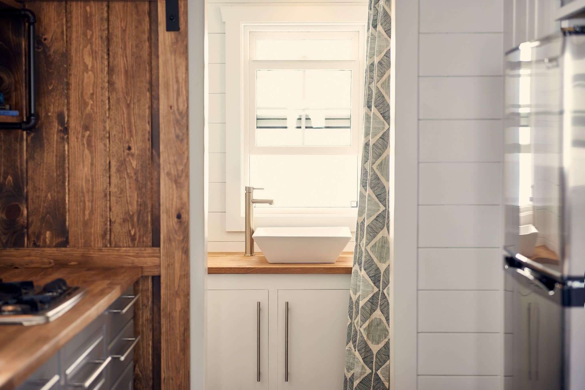 Brushed nickel single-handle faucet installed on wooden countertop above white vessel sink in modern bathroom.