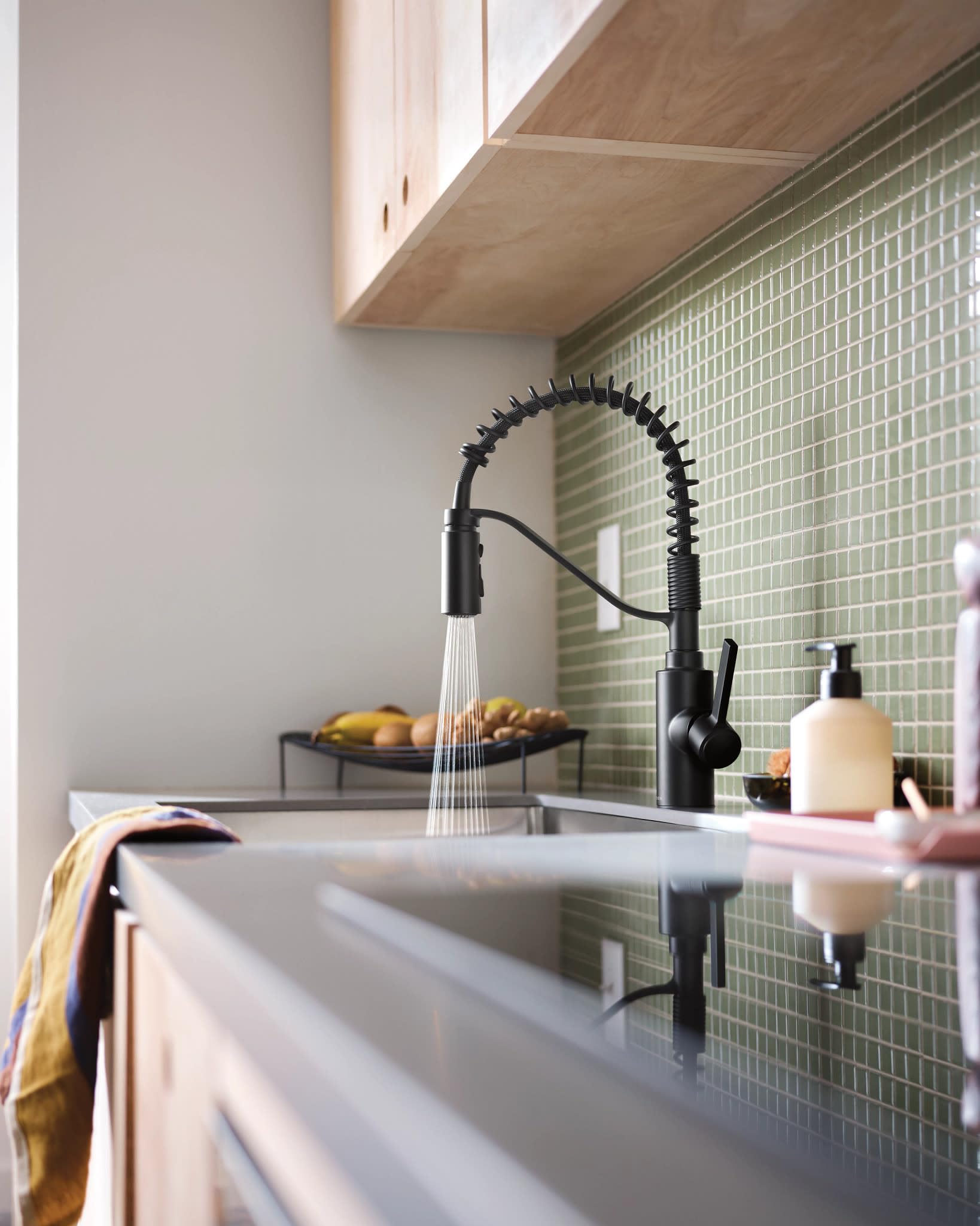 Matte black pull-down kitchen faucet with coiled spring hose and single handle mounted above white sink.