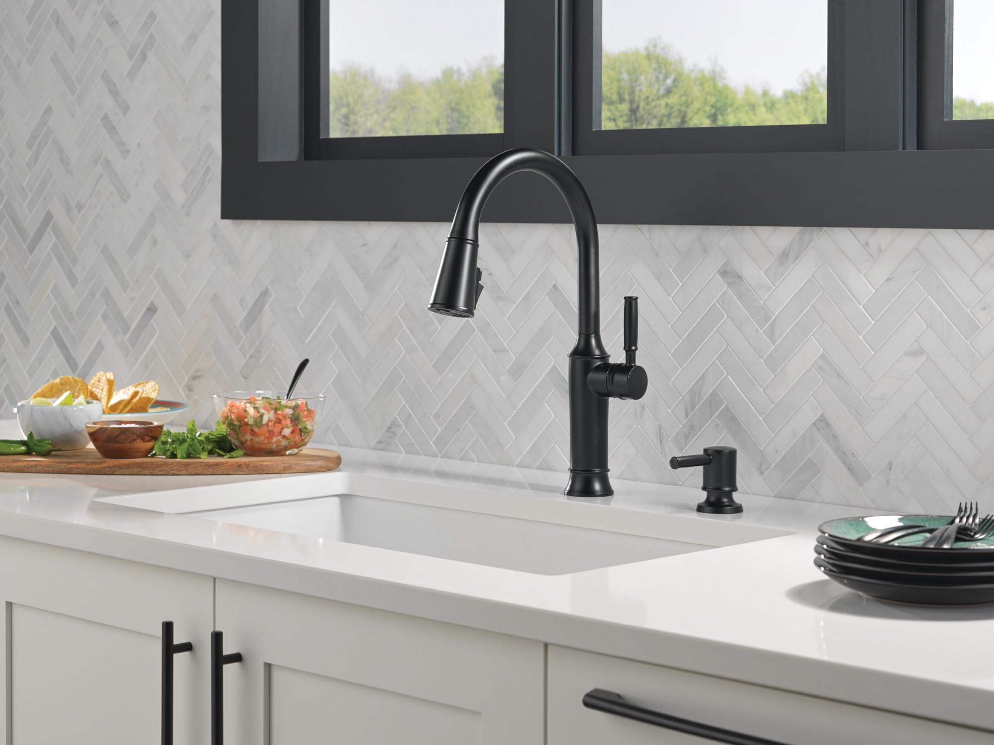 Matte black metal soap dispenser with cylindrical pump on white kitchen counter next to sink faucet.