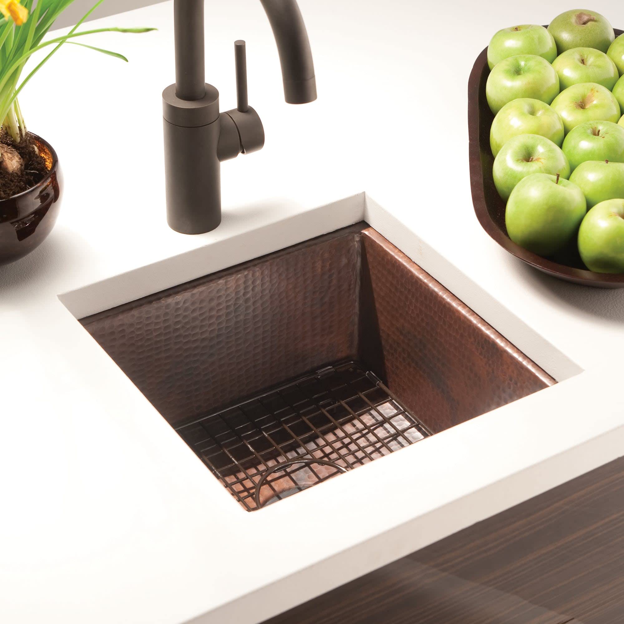Polished copper prep sink with hammered interior, black faucet, and drain grid in countertop setting.