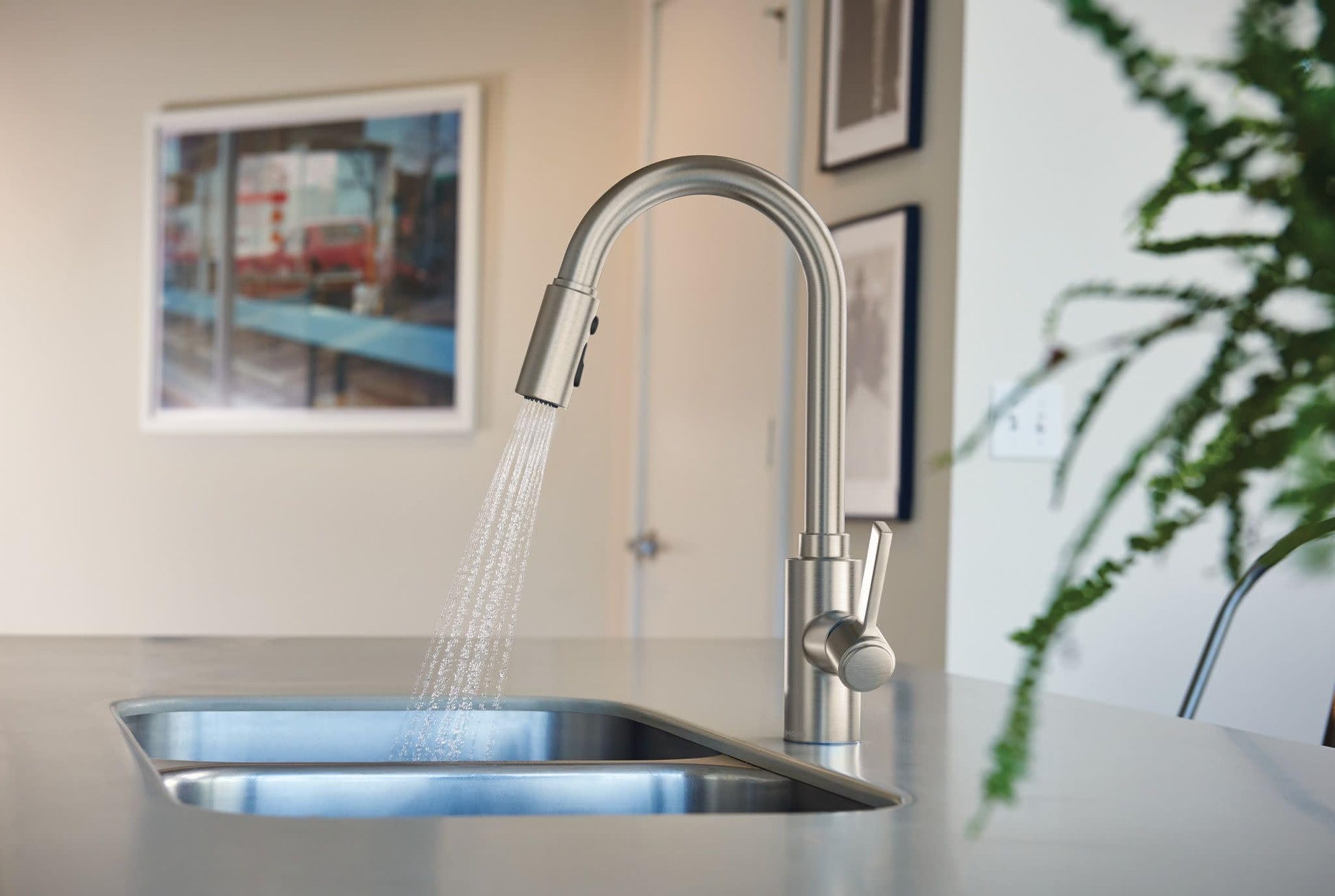 Stainless steel kitchen faucet with curved spout and pulldown sprayer head extended over rectangular sink.