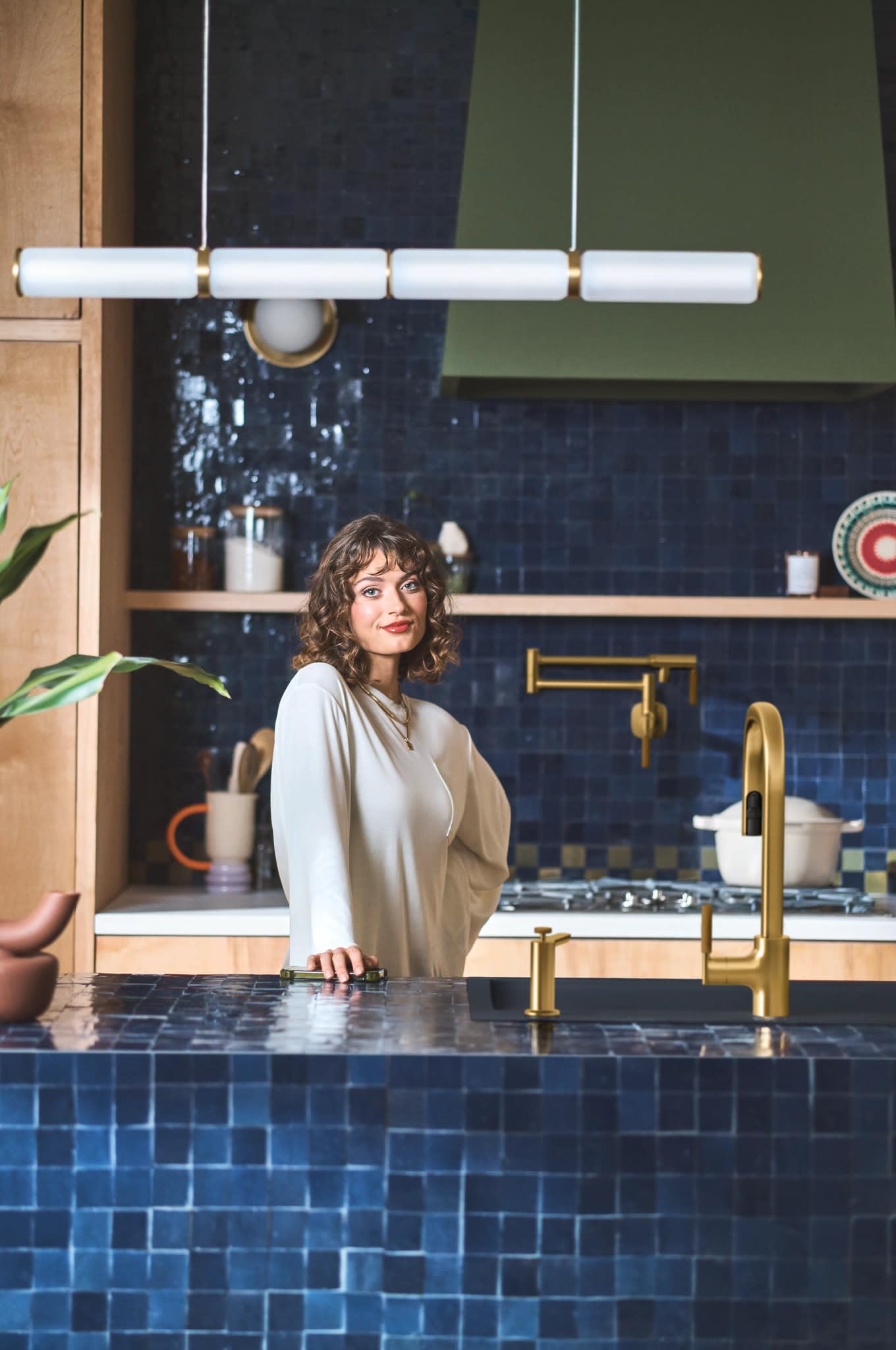 Brushed gold pulldown kitchen faucet with single handle installed above blue tile sink in modern kitchen.