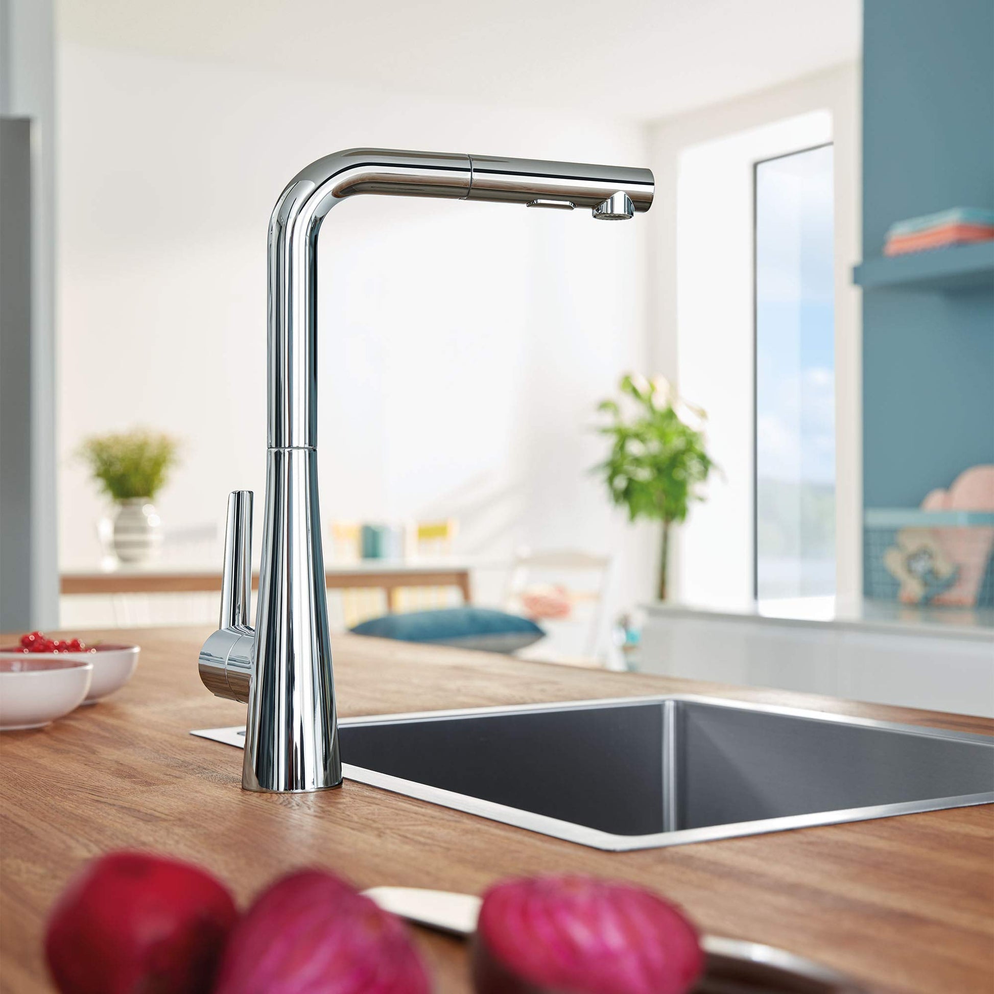 Polished chrome single-handle pull-out kitchen faucet with tall curved spout positioned above stainless steel sink.
