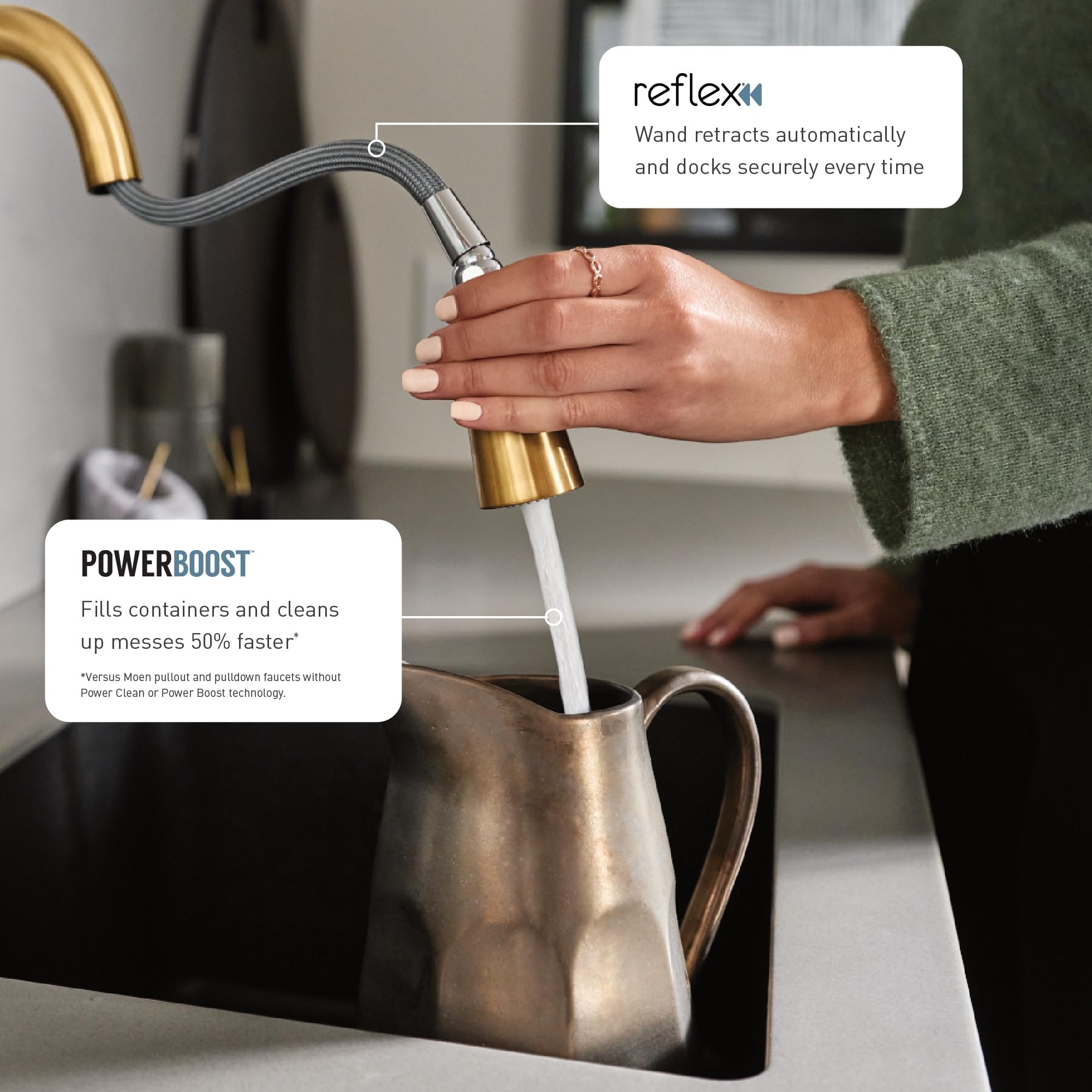 Brushed gold kitchen faucet with pulldown spray wand extended over a metal pitcher, hand operating the single handle.