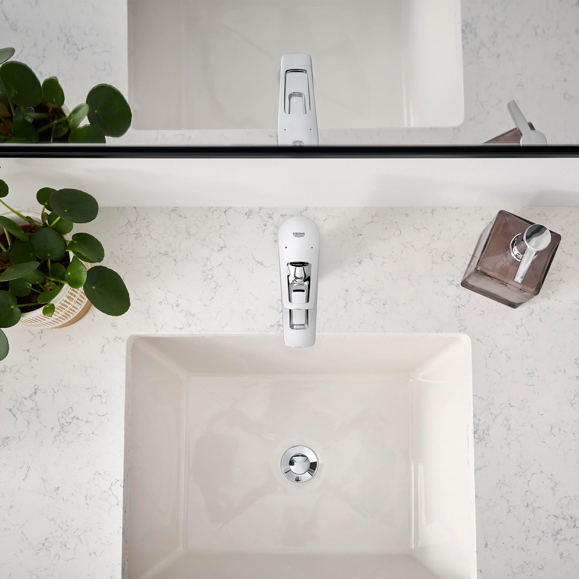 Chrome single-handle bathroom faucet with rectangular spout mounted on white rectangular sink in marble countertop.