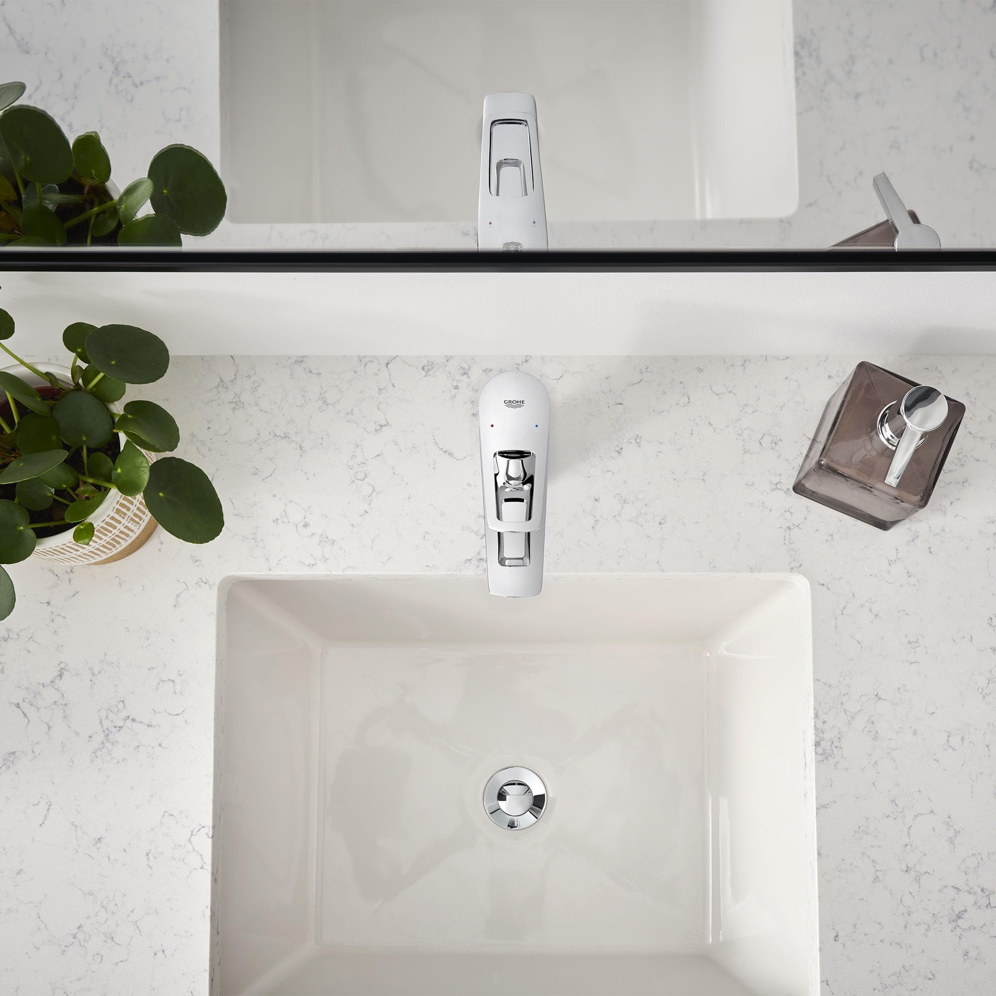 Chrome single-handle bathroom faucet with rectangular spout mounted on white rectangular sink in marble countertop.