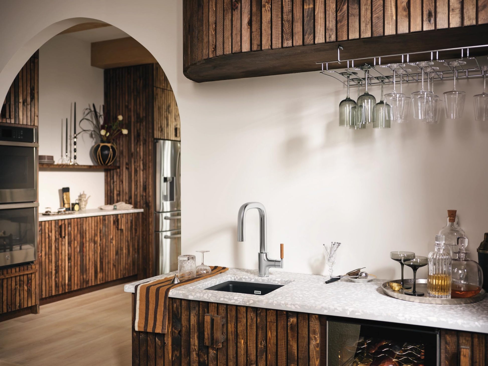 Chrome single-handle bar faucet with pulldown sprayer mounted on white countertop in modern kitchen.