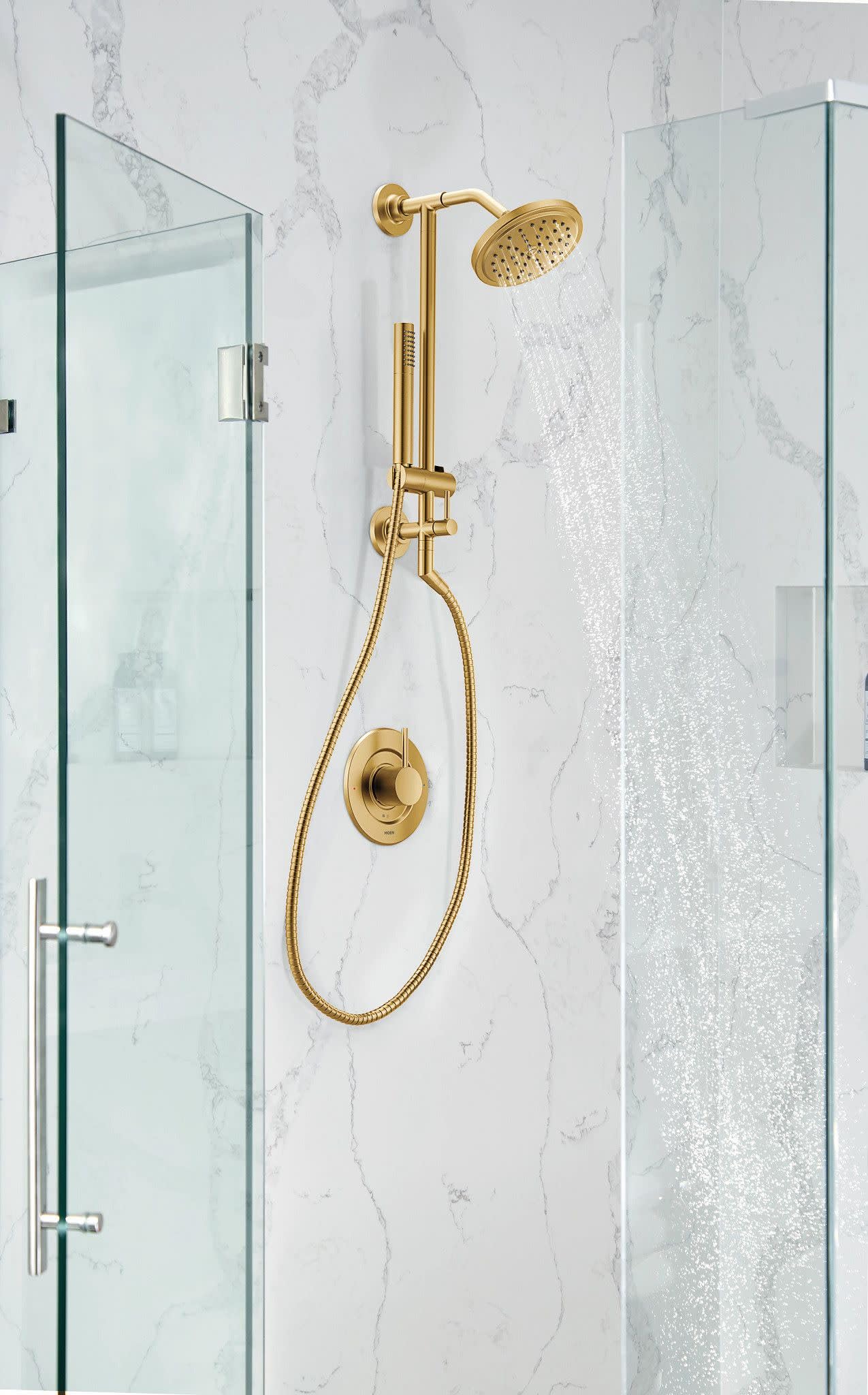 Brushed gold shower system mounted on marble wall with overhead rainshower head, handheld wand, and valve control between gla
