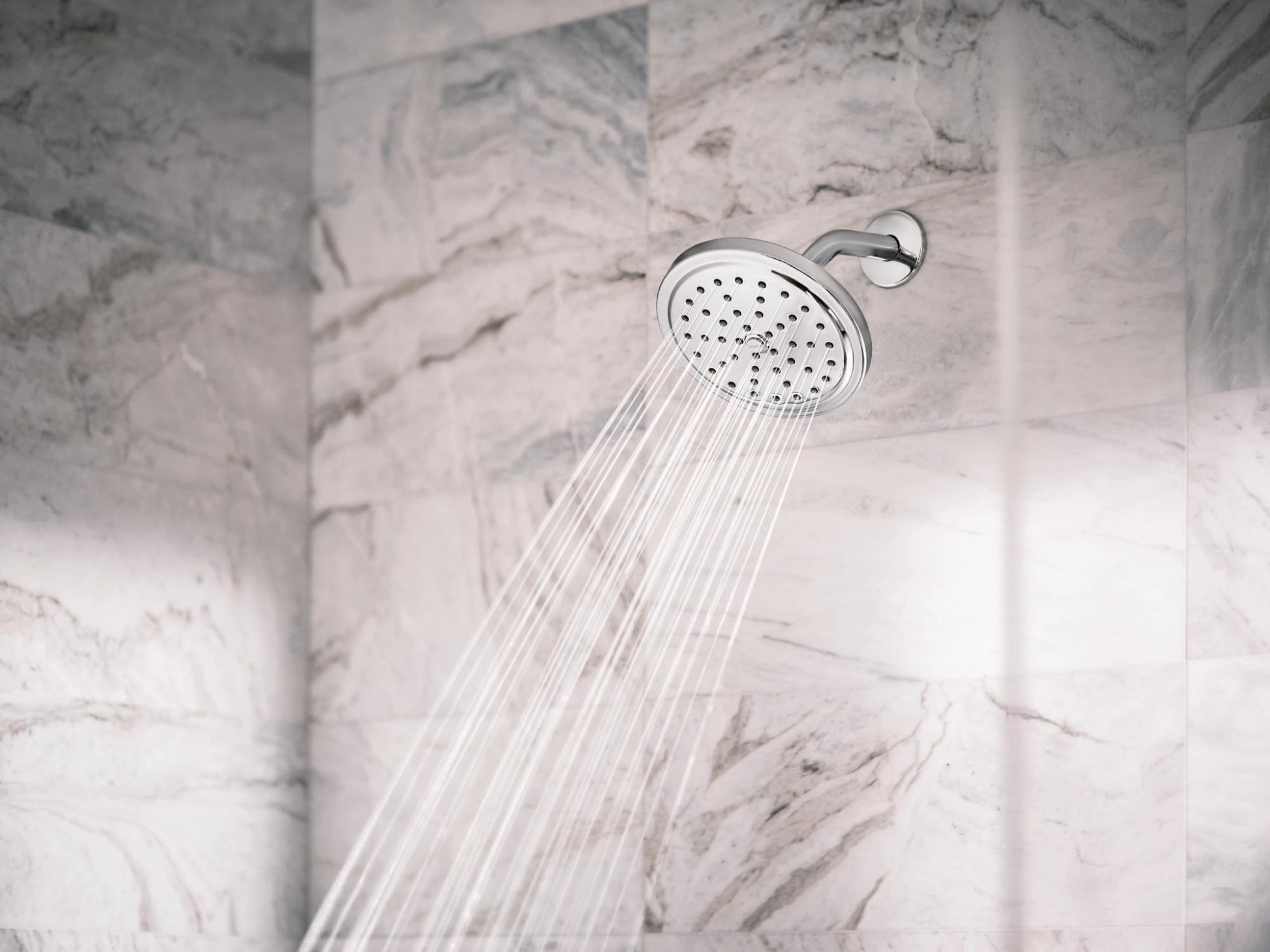 Chrome showerhead with multiple spray jets mounted on marble tile wall.