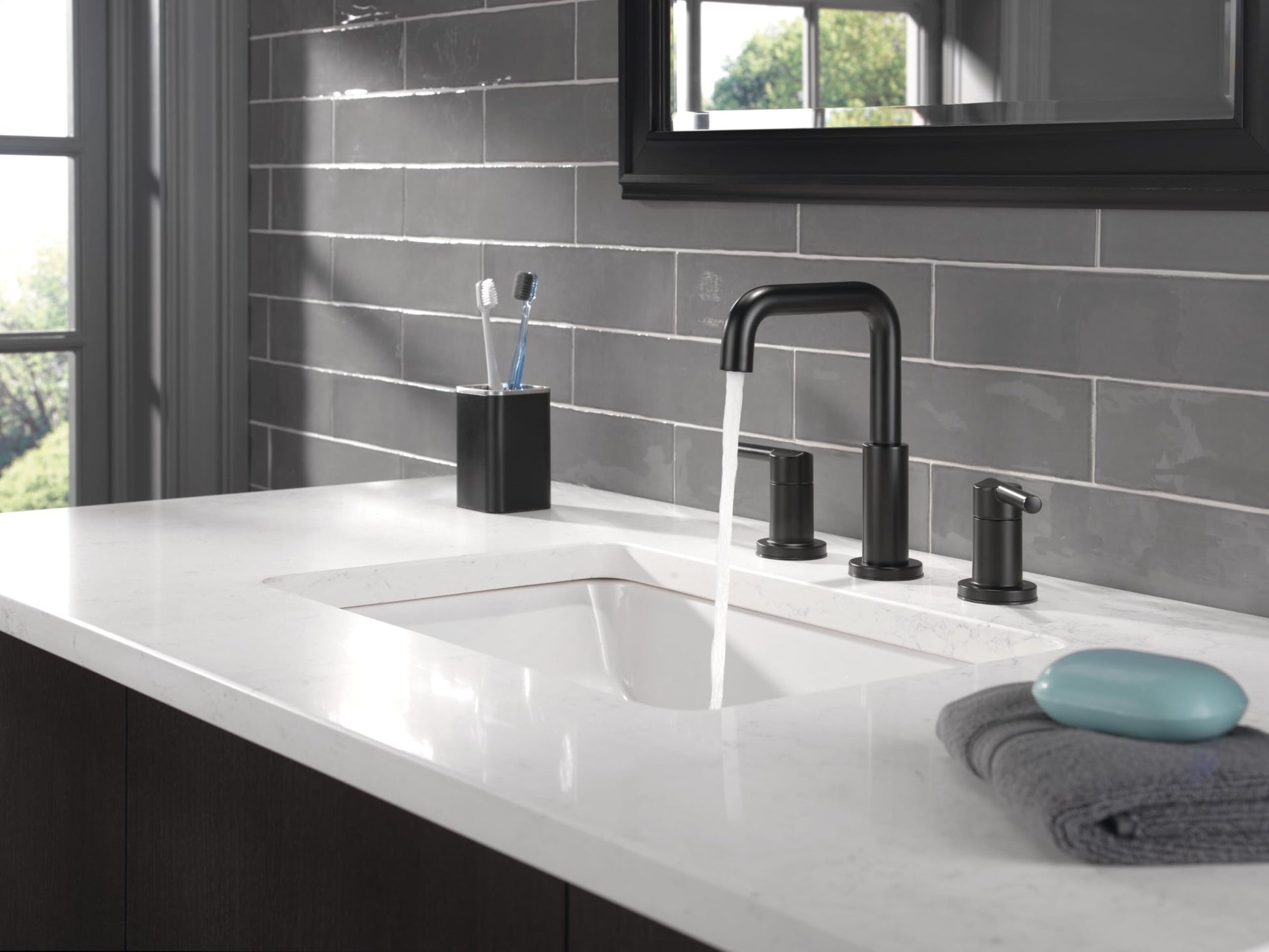 Matte black two-handle widespread bathroom faucet with arched spout installed on white countertop above sink.