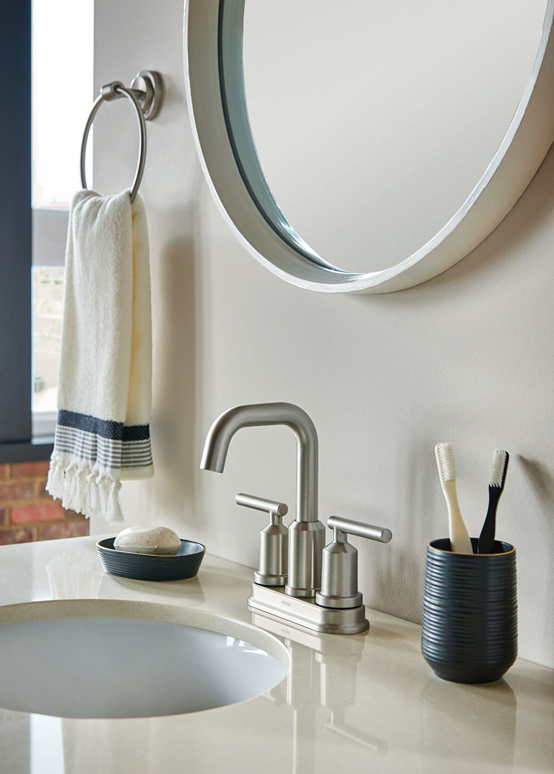 Brushed nickel wall-mounted towel ring holding a striped hand towel above a bathroom sink.