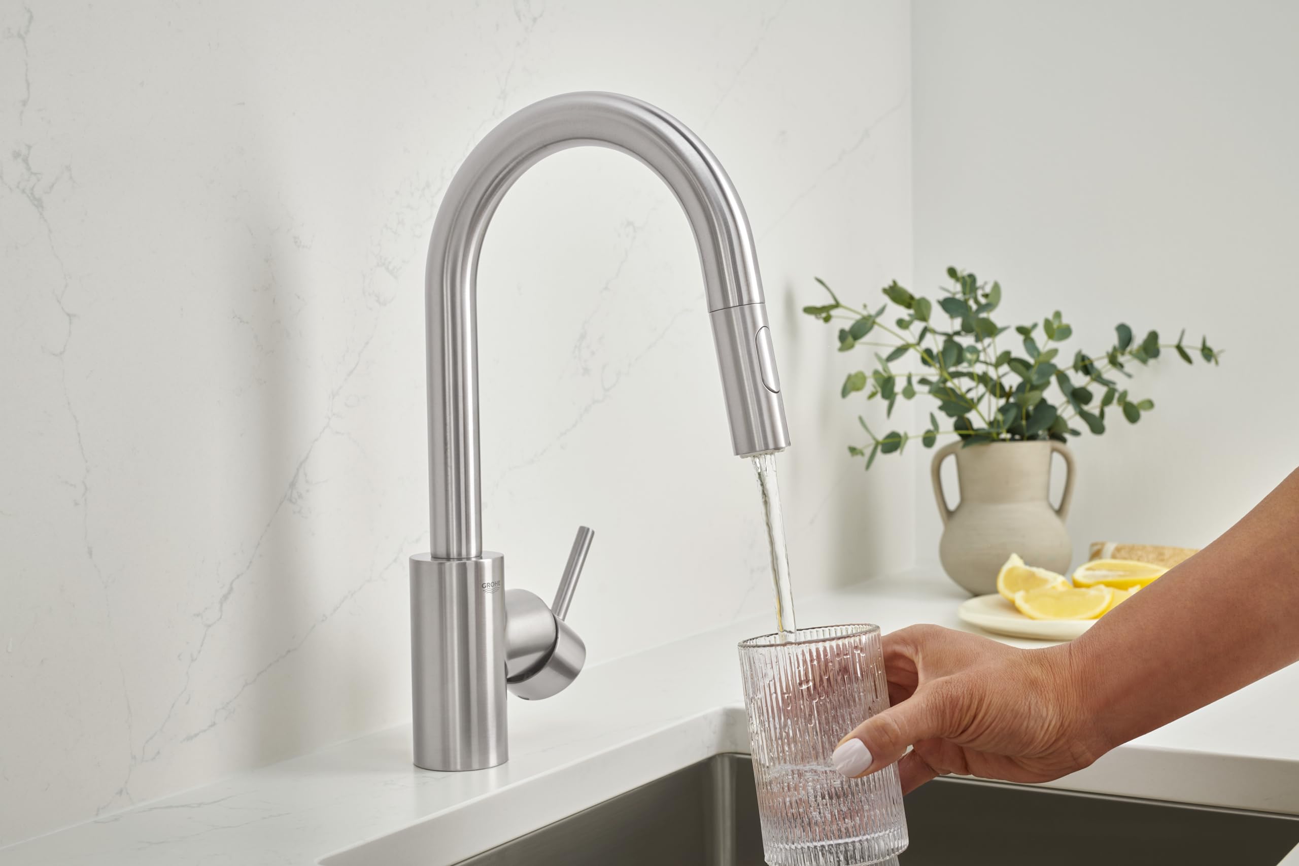 Stainless steel single-handle pull-down faucet with curved spout over sink, dispensing water into glass.