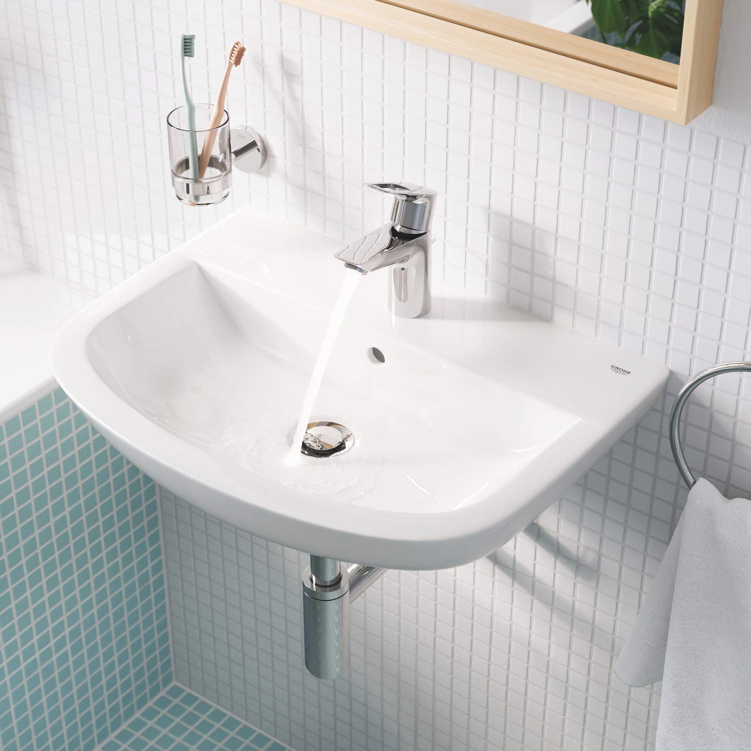Chrome holder mounted on bathroom wall above sink, holding clear glass with toothbrushes.