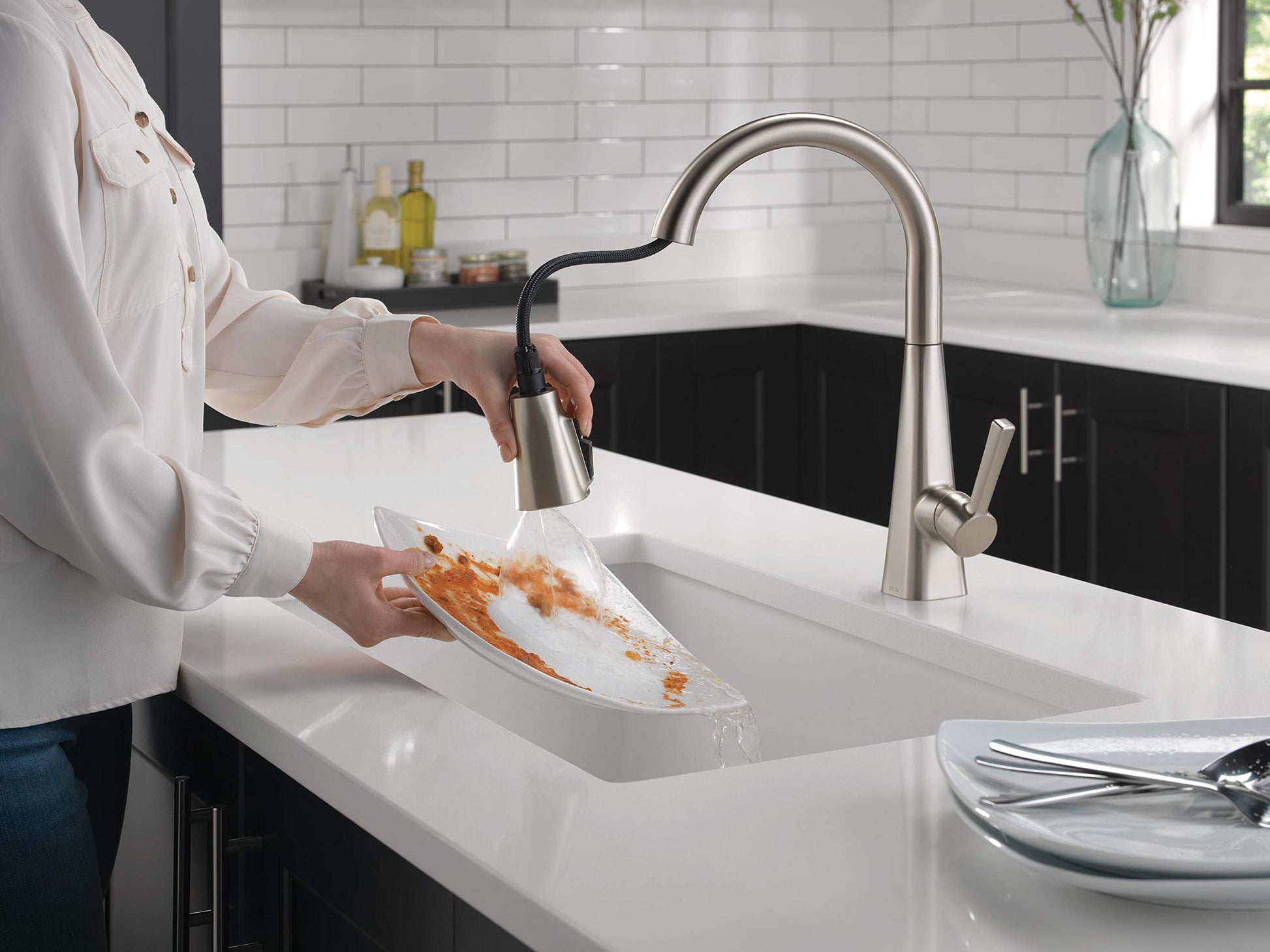 Stainless steel pull-down kitchen faucet with single handle shown rinsing food debris from a plate over a white sink.