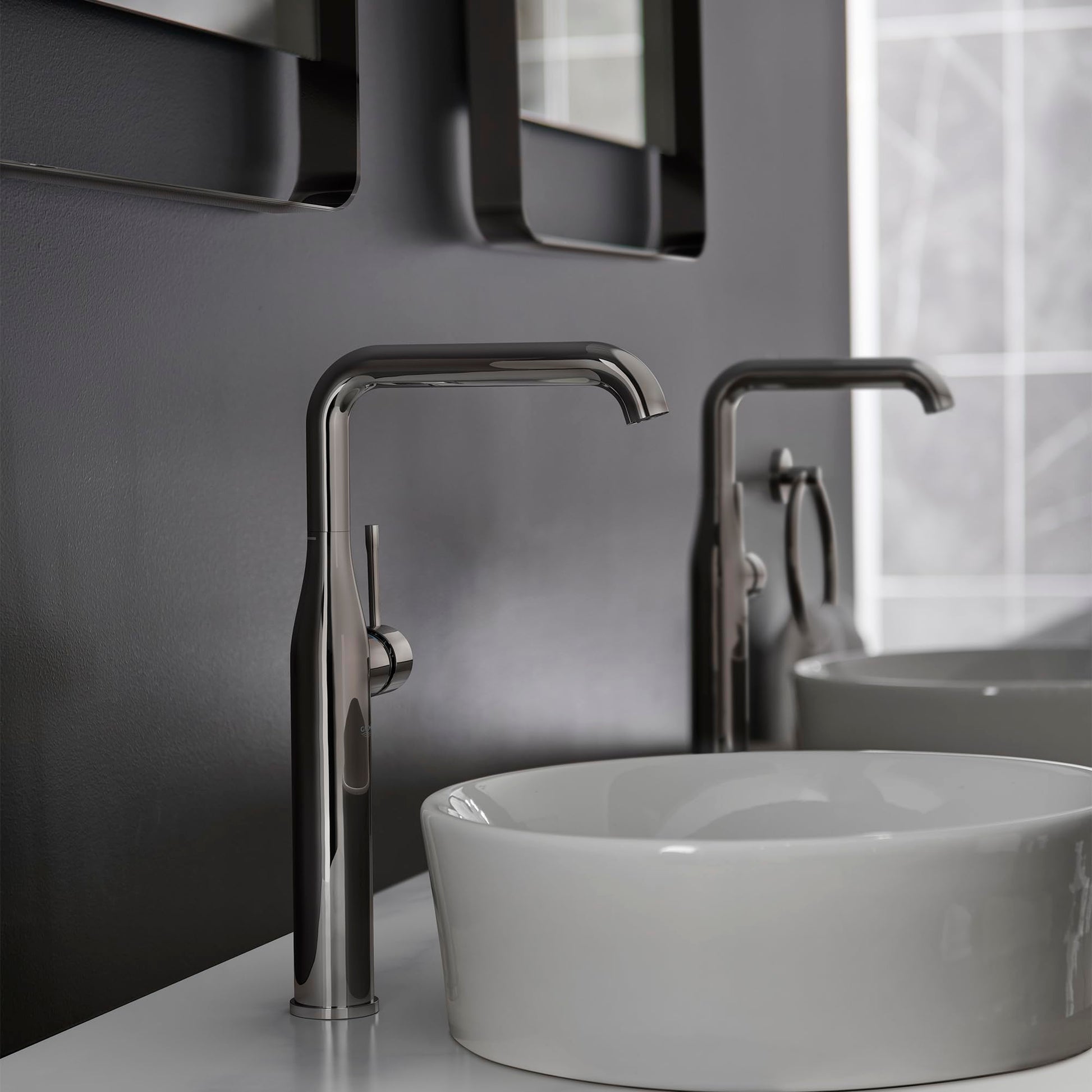 Dark graphite single-handle faucet with tall curved spout mounted next to white round vessel sink.