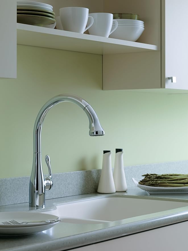 Chrome high-arc kitchen faucet with pull-down spray head installed above white sink in kitchen.