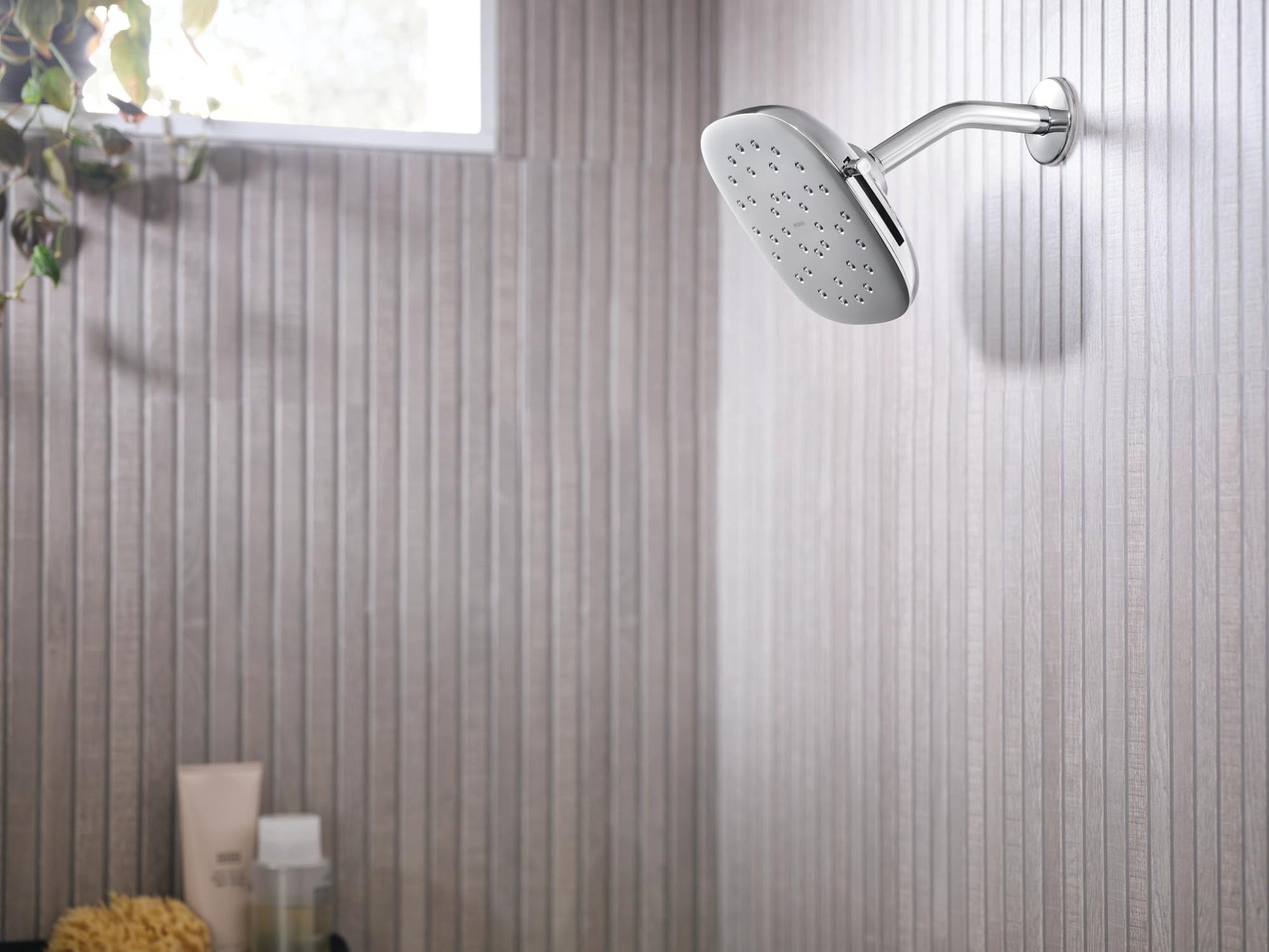 Chrome square rain shower head with multiple spray holes mounted on curved arm against textured bathroom wall.