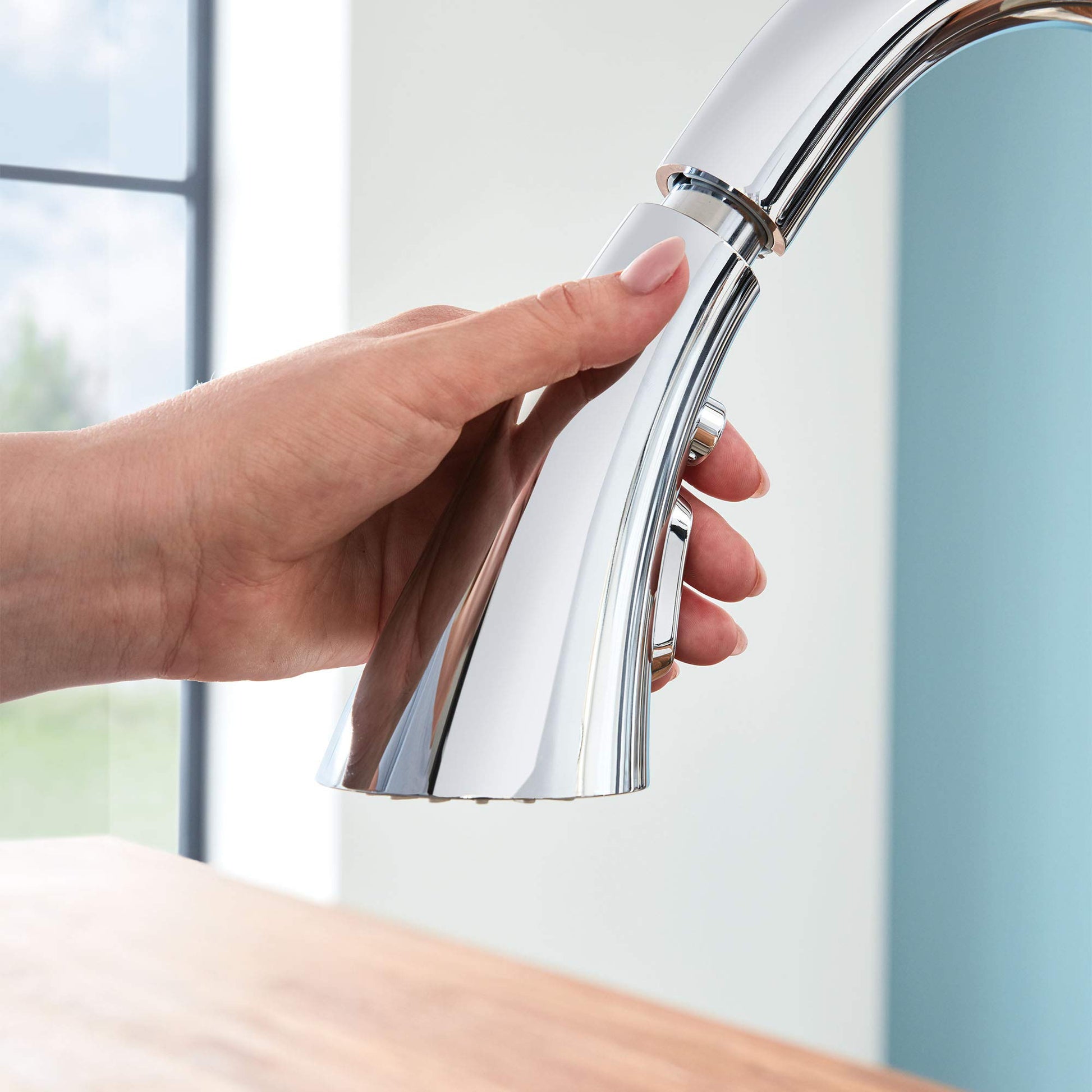 Chrome pull-down kitchen faucet with single handle and spray head being held over sink.