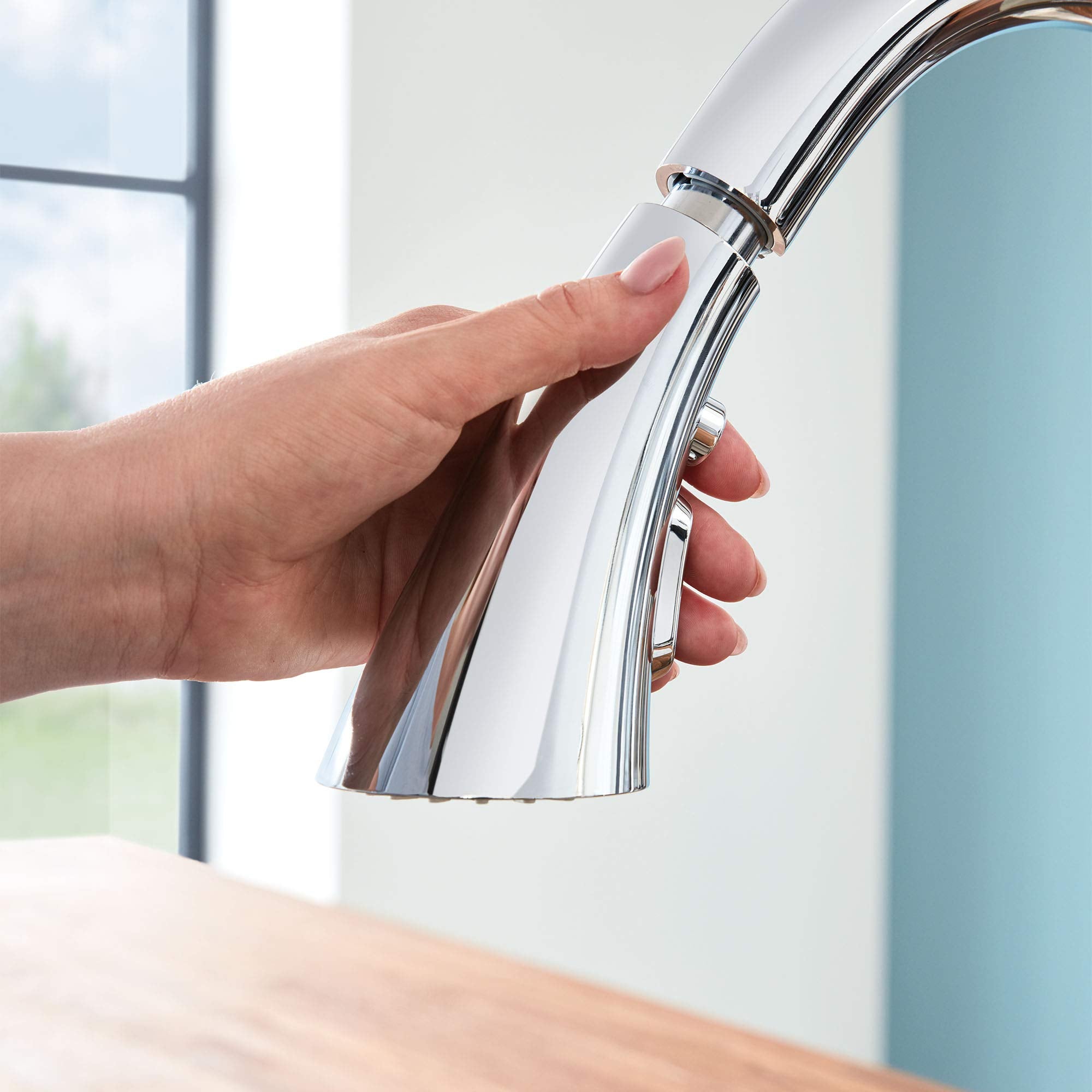 Chrome pull-down kitchen faucet with single handle and spray head being held over sink.