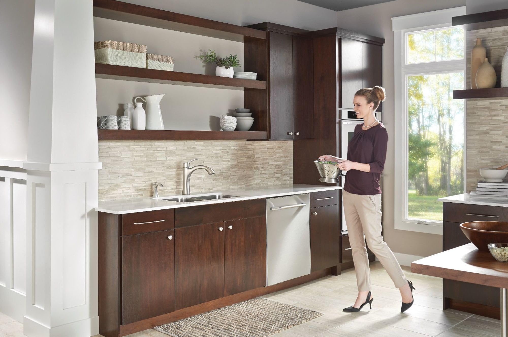 Stainless steel deck-mounted soap dispenser with refillable bottle mounted above sink in transitional kitchen.