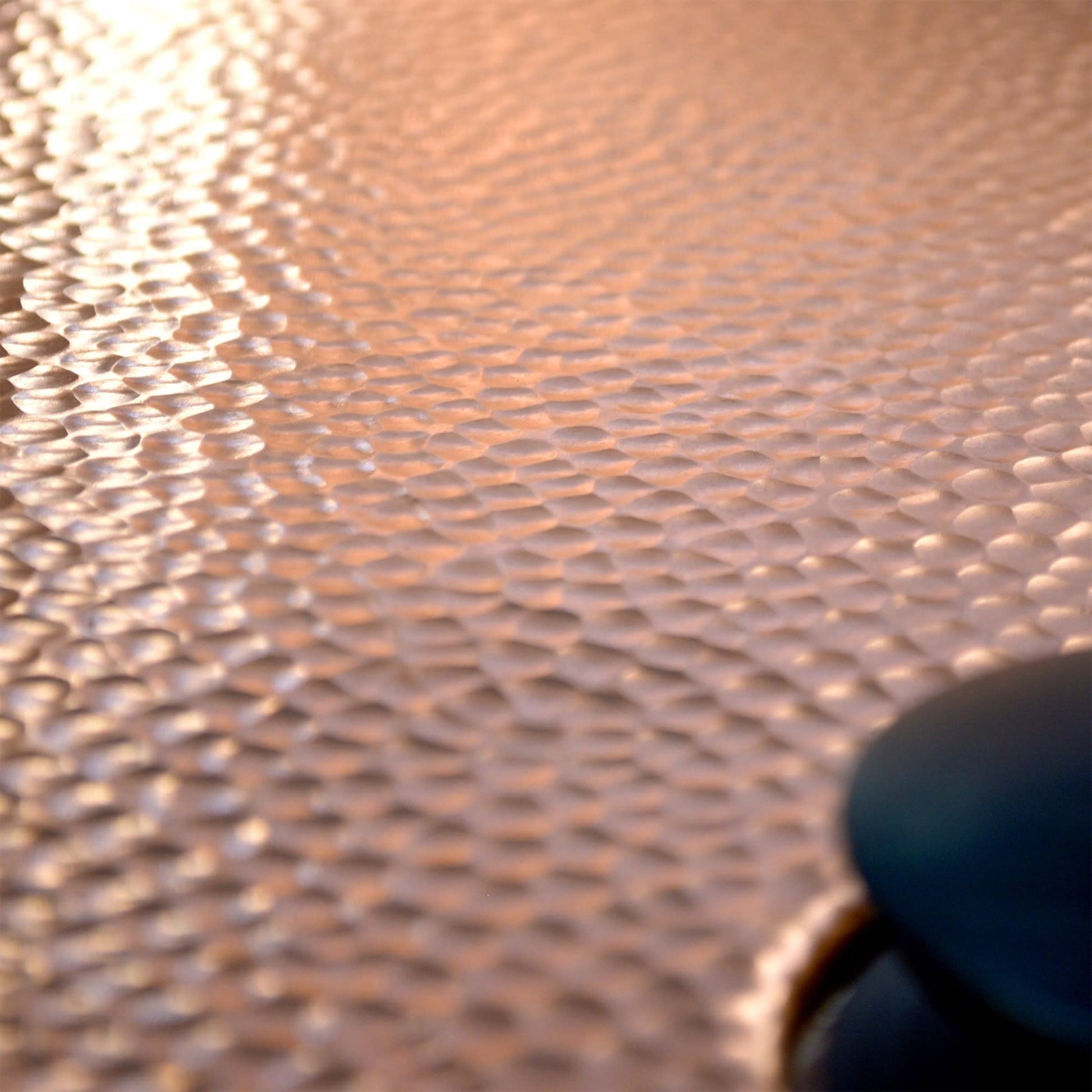 Closeup of hammered copper bathtub surface with textured finish and brushed nickel detail visible at edge.