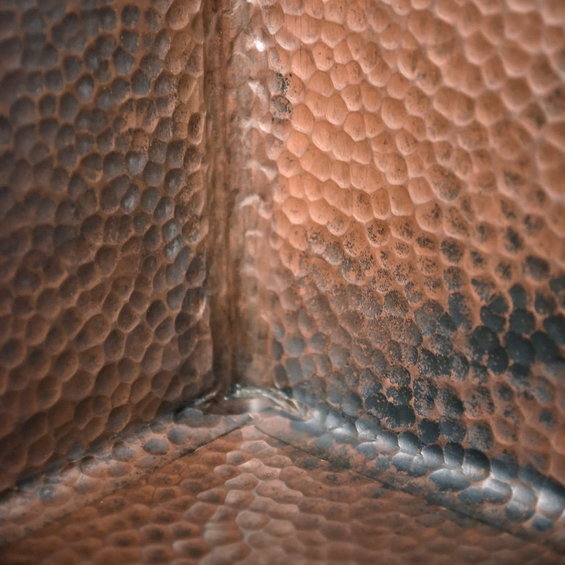 Close-up of antique copper sink interior corner showing hammered texture and patina finish.