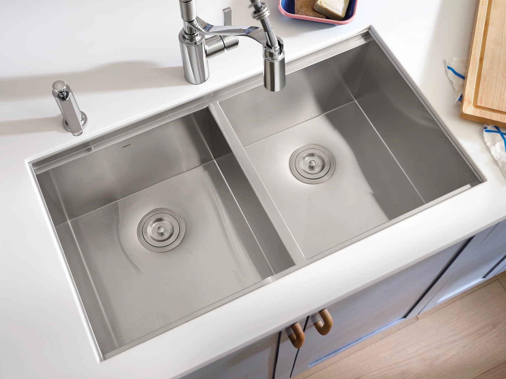 Stainless steel double bowl undermount sink with two drains and faucet installed in white countertop.