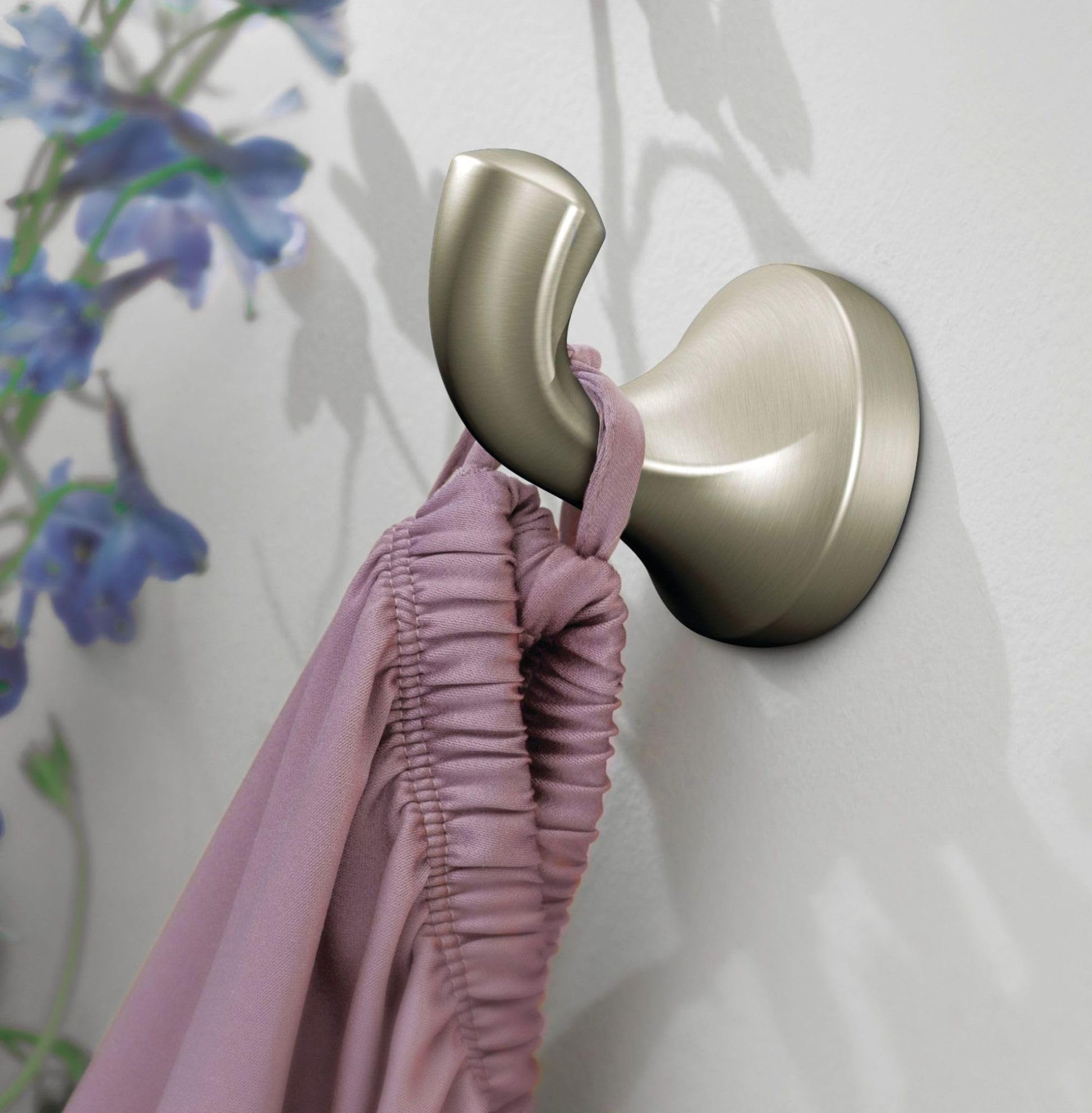 Brushed nickel wall-mount robe hook with curved hook arm holding a pink fabric.