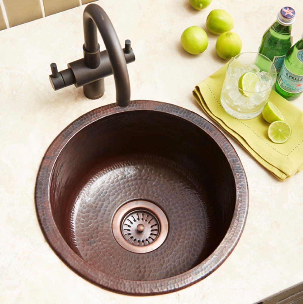 Hammered copper circular bar sink with integrated drain, paired with dark bronze faucet and side sprayer.