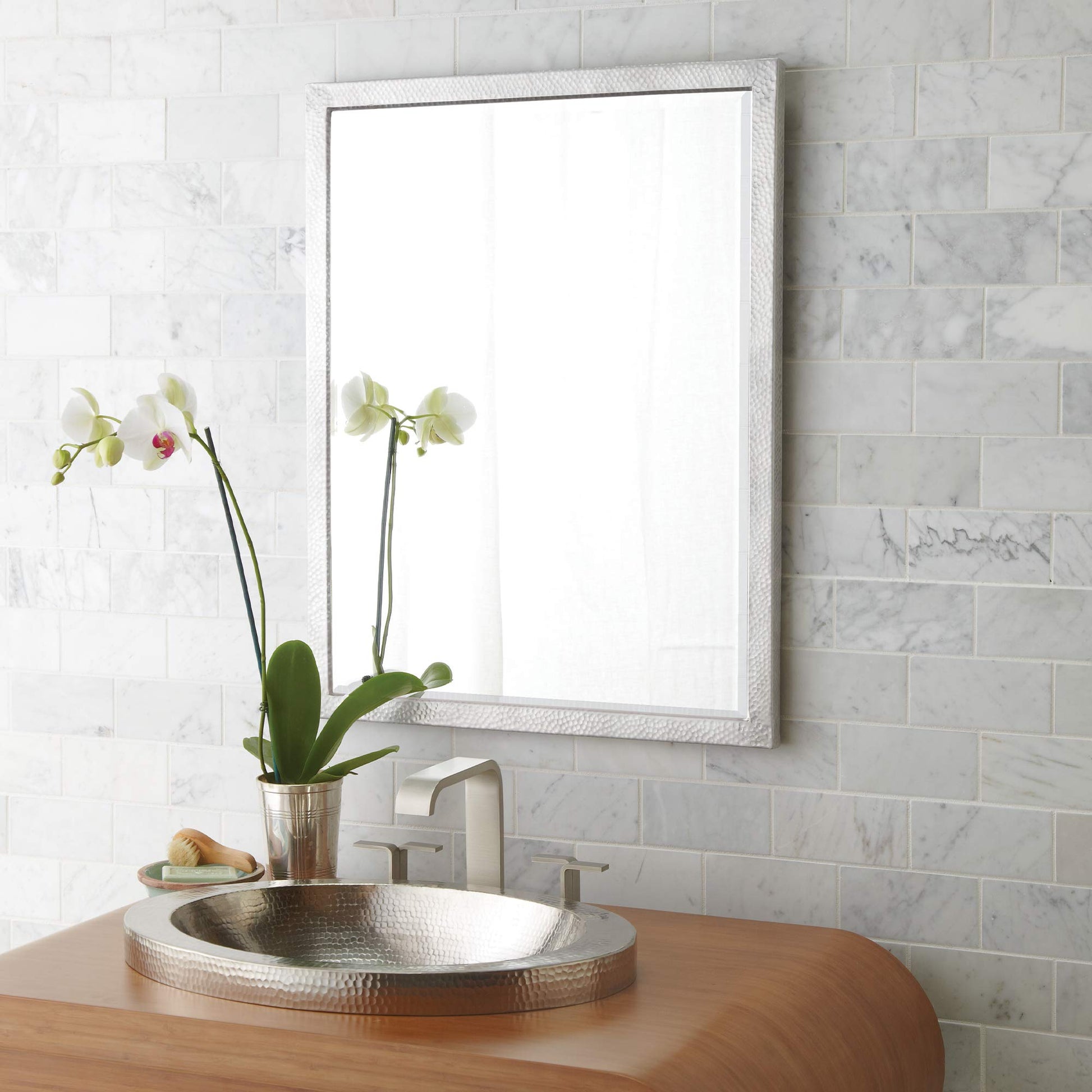 Rectangular wall mirror with white textured frame mounted above bathroom sink with marble tile backsplash.